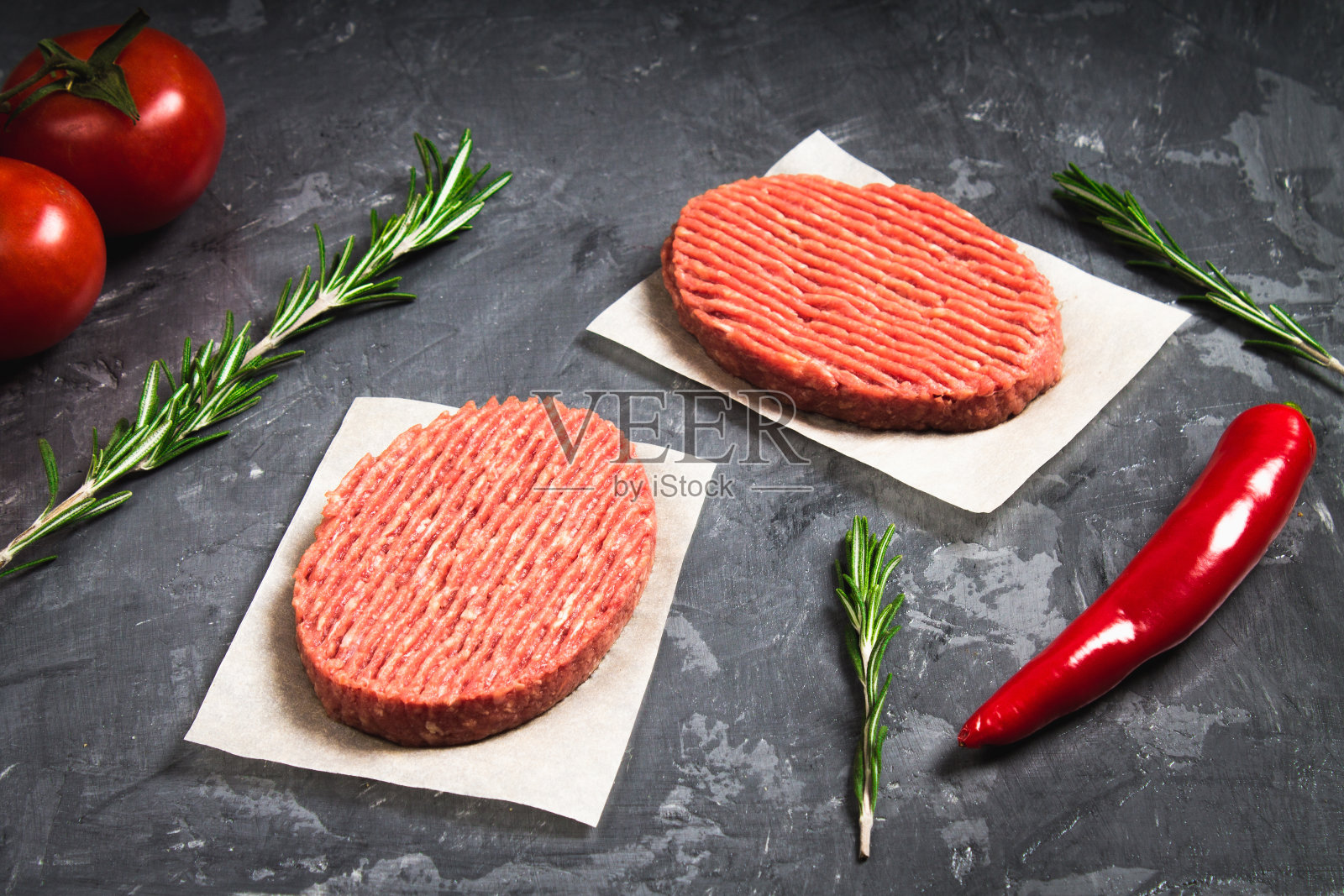 烤牛皮纸上的生汉堡配上西红柿，辣椒和照片摄影图片