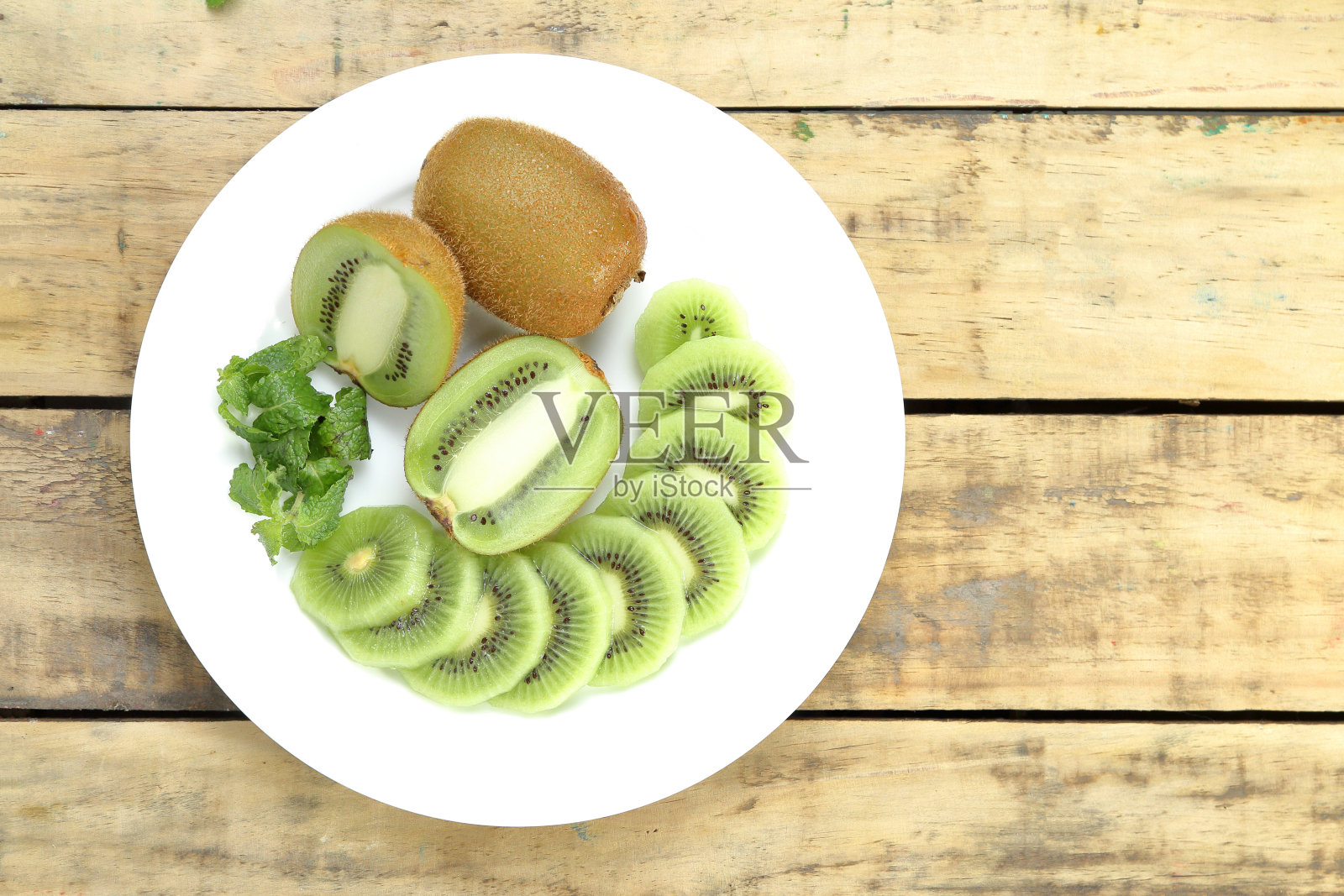 将猕猴桃切片放在白色盘子上，木板为背景。从以上观点。照片摄影图片