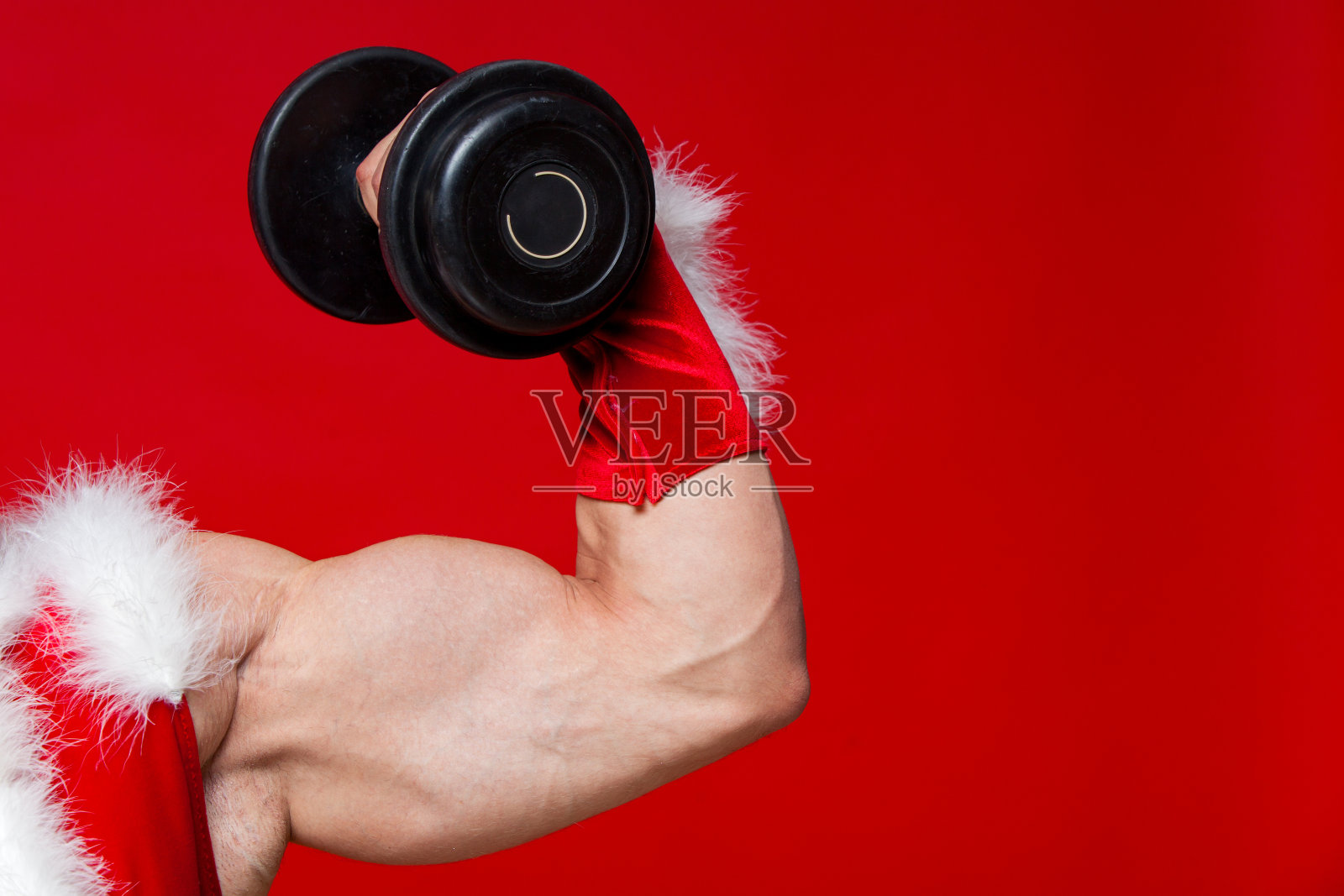 节日和庆祝活动，新年，圣诞节，体育，健身，健康的生活方式-肌肉英俊性感的圣诞老人。孤立在红色背景上。显示了一个大的二头肌。特写镜头照片摄影图片