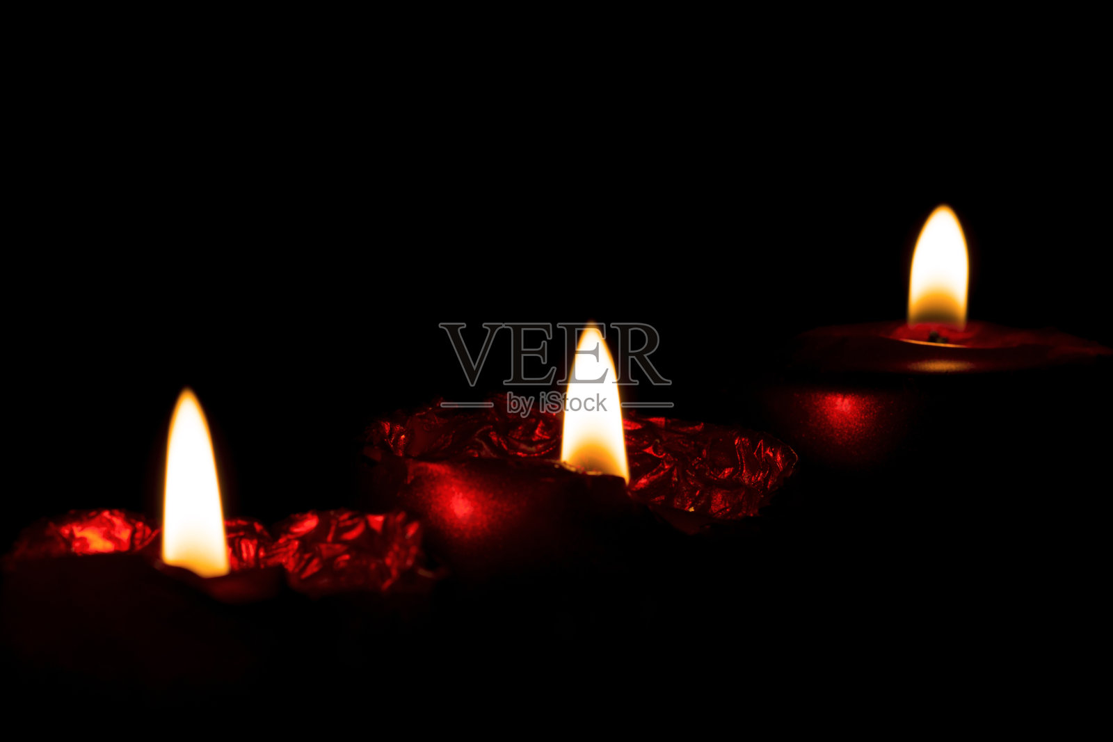 一排三个燃烧的红色蜡烛在黑暗中与模糊的背景和前景的特写照片摄影图片