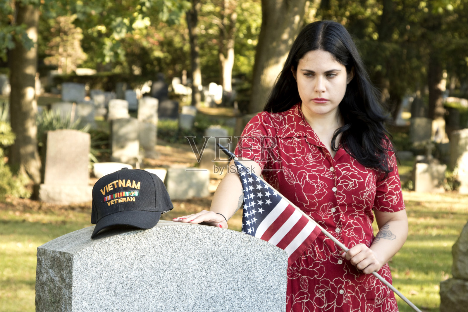 一名年轻女子坐在墓碑前看着越战老兵的徽章，背景是墓碑照片摄影图片