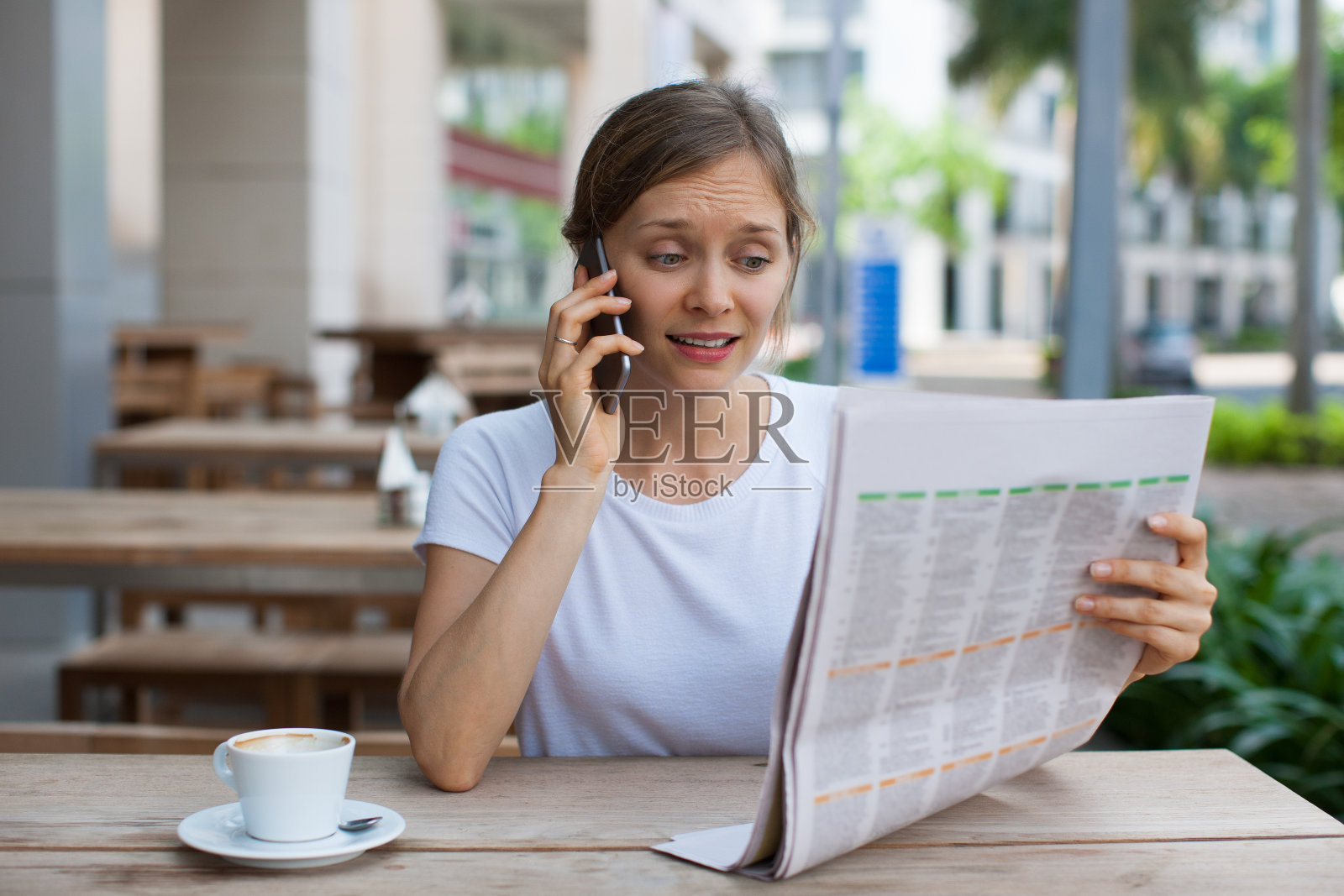 忧心忡忡的女人拿着报纸打电话来照片摄影图片