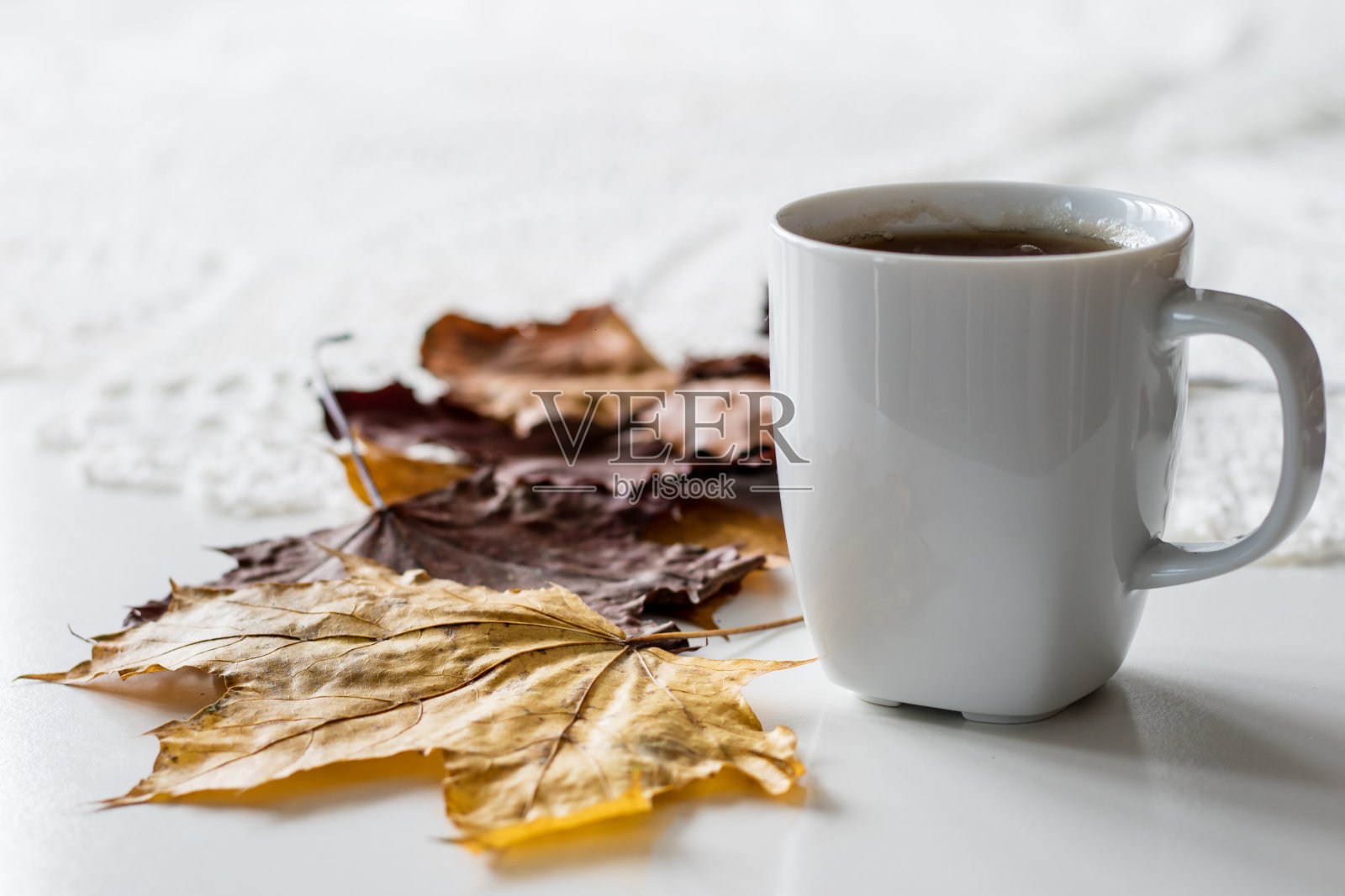 秋天的一天，一杯可口的茶和蛋糕。旁边是干燥的枫叶和山毛榉。厨房的桌子上。白色的台面。照片摄影图片