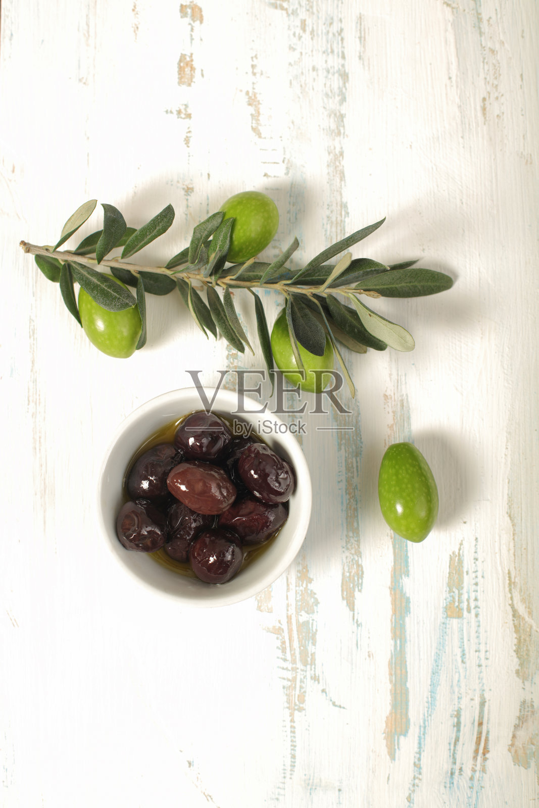 瓷碗里的橄榄和木制背景上的年轻橄榄枝照片摄影图片