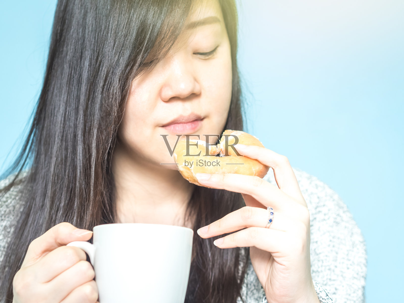 正面视图从亚洲妇女的手与布持有白色咖啡杯和吃甜甜圈早上时间与蓝色柔和的背景照片摄影图片