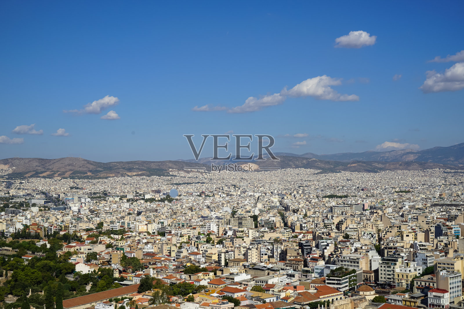 从雅典卫城看雅典城，显示白色的建筑，山，树，蓝天和白云的背景照片摄影图片