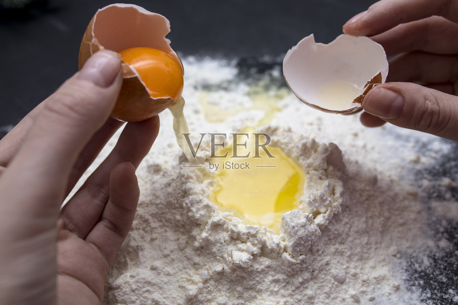 女性面包师的手打碎鸡蛋成生面团的特写。烘焙和食品准备的概念。照片摄影图片