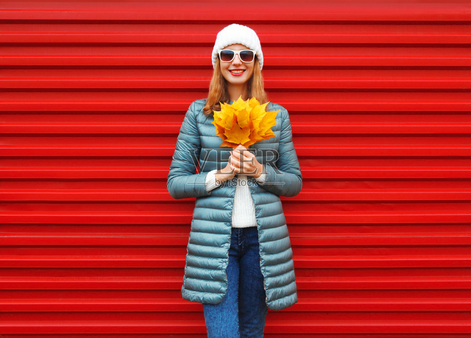 在城市的红色背景上，时尚的秋日微笑的女人手里拿着黄色的枫叶照片摄影图片