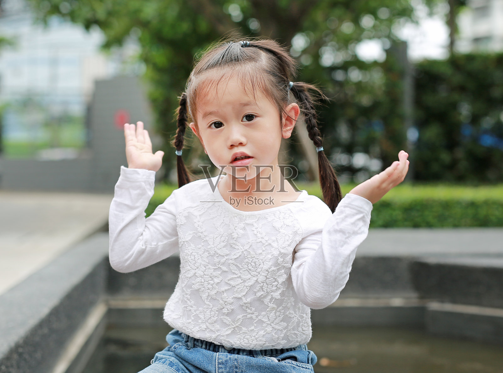 在花园里张开手臂的小女孩的肖像。照片摄影图片