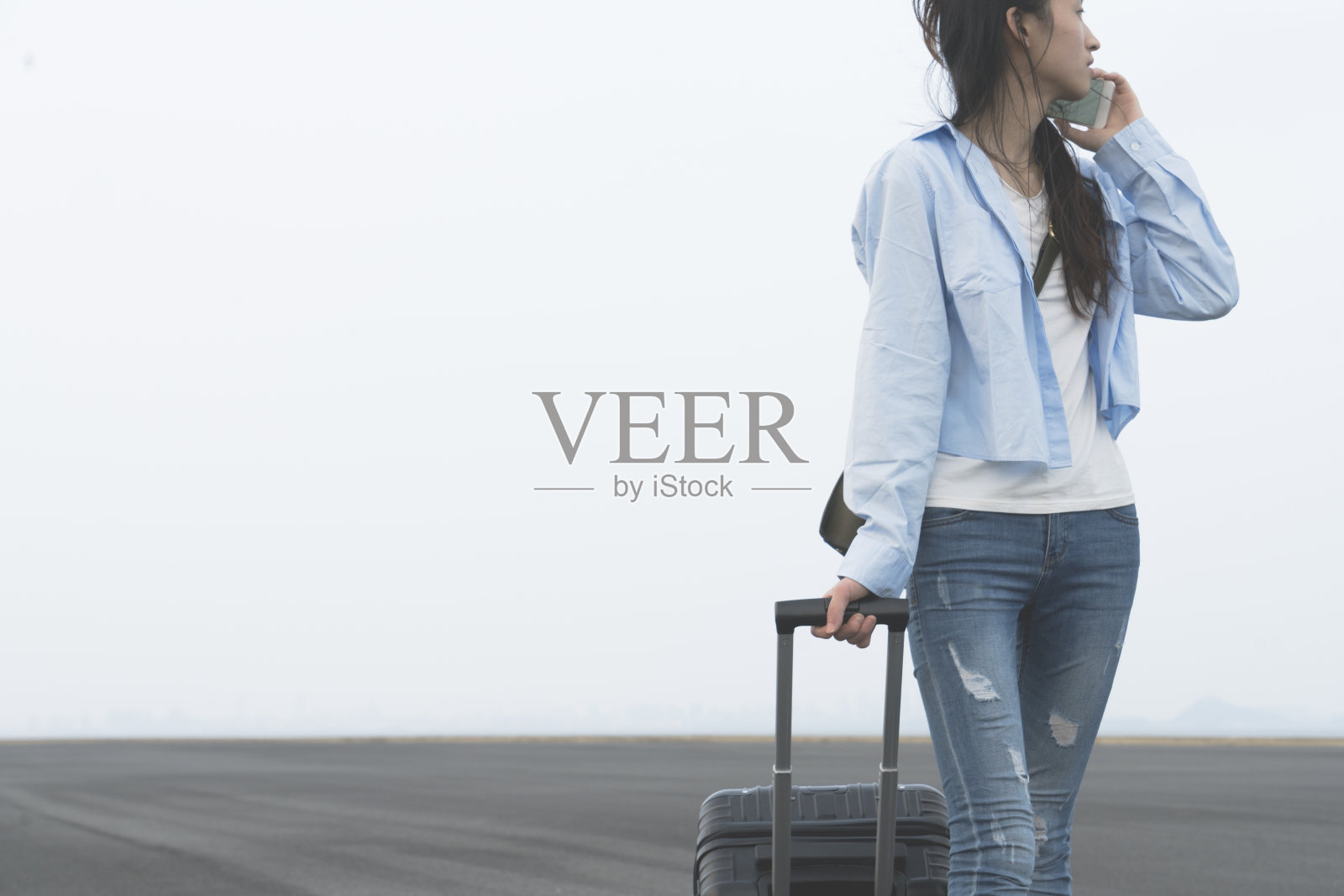 年轻女子拿着行李箱走路，用手机打电话照片摄影图片