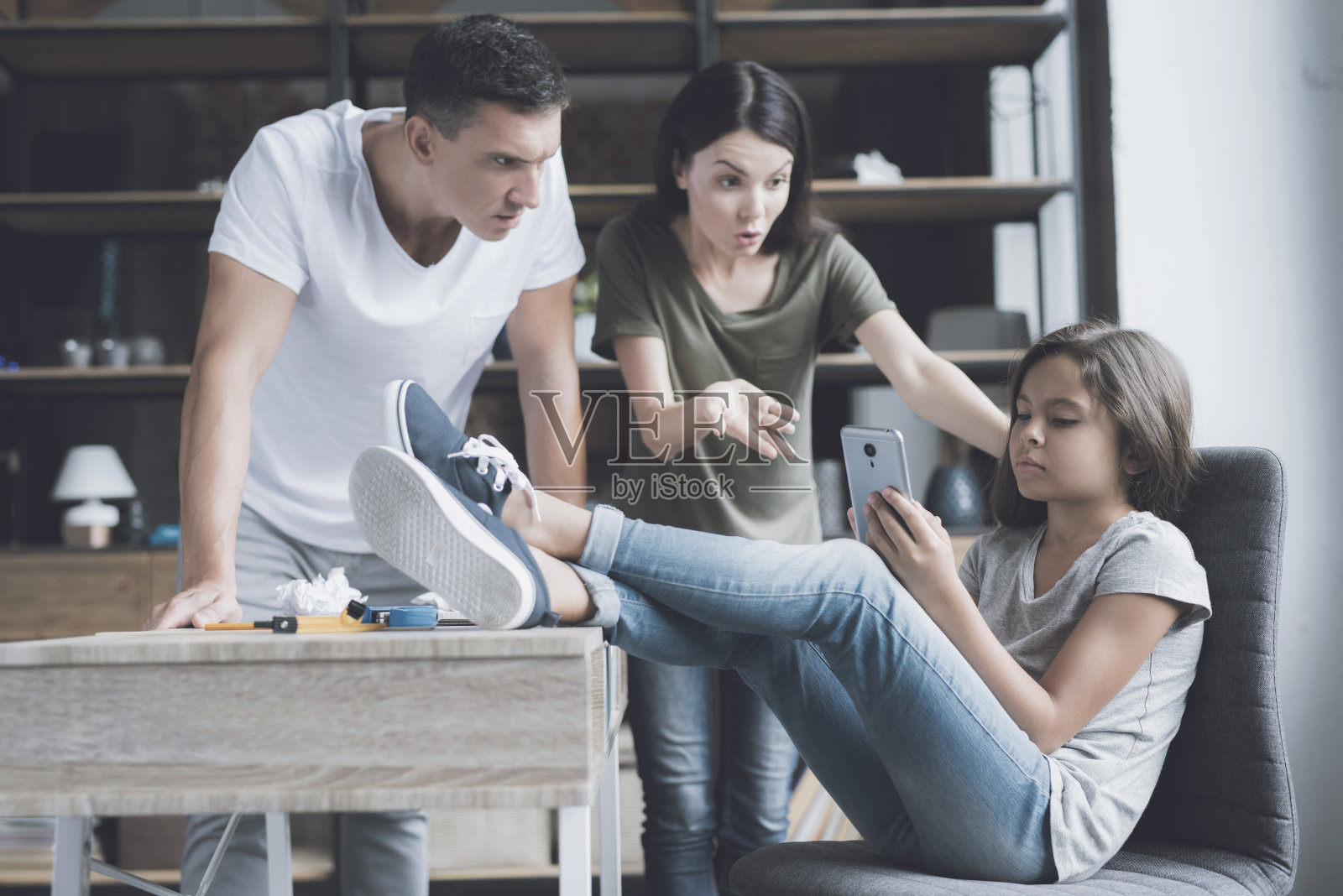 父母责骂把腿搭在桌子上、不理睬他们的小女儿照片摄影图片