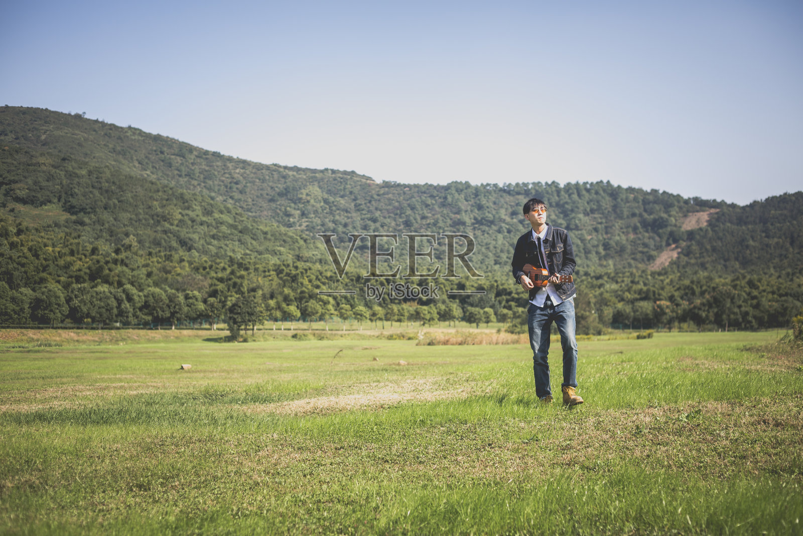 一个精力充沛的年轻人在一个阳光明媚的日子里弹着小吉他照片摄影图片