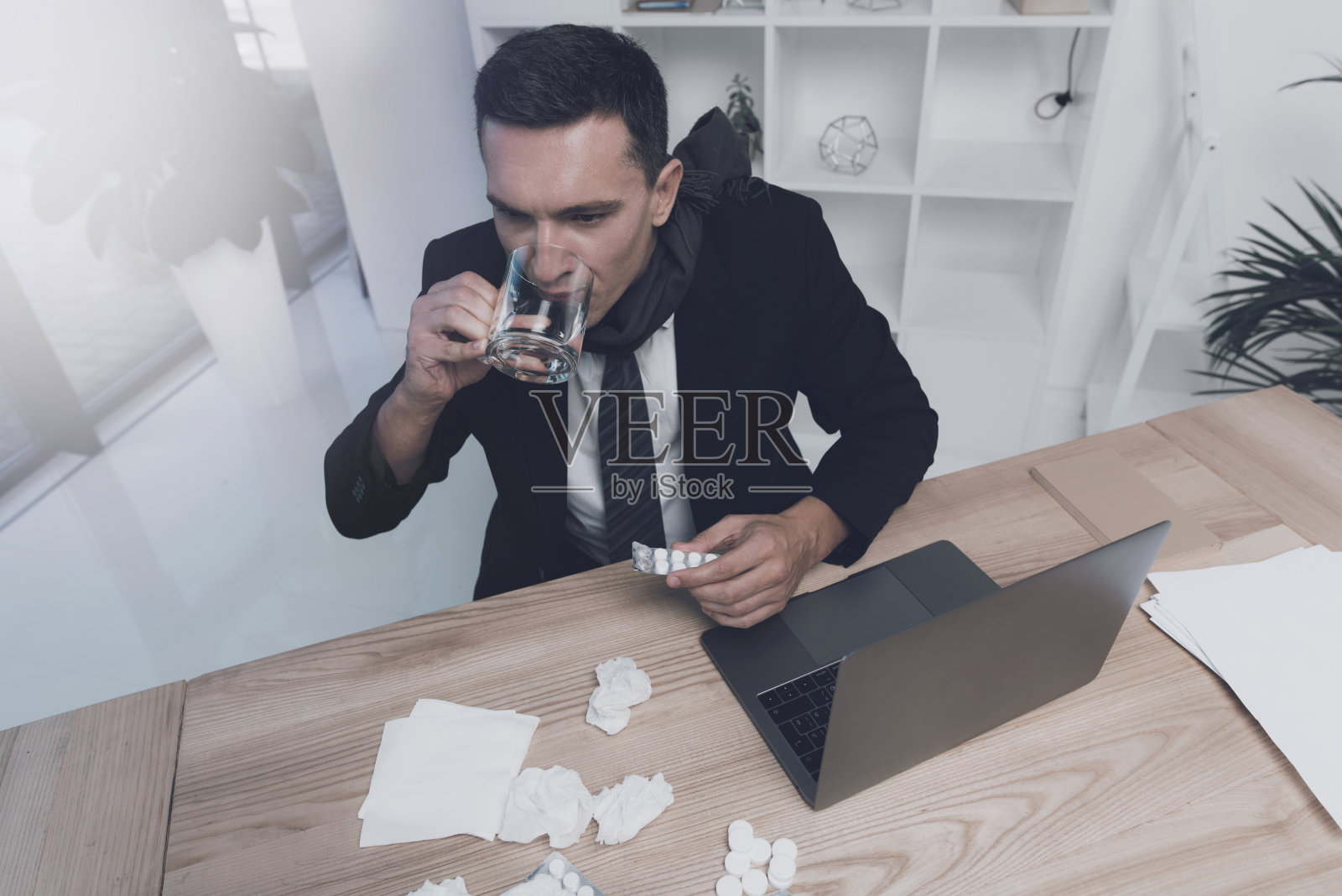 一个病人正坐在办公室里他工作的地方。他手里拿着一颗药丸和一杯水照片摄影图片