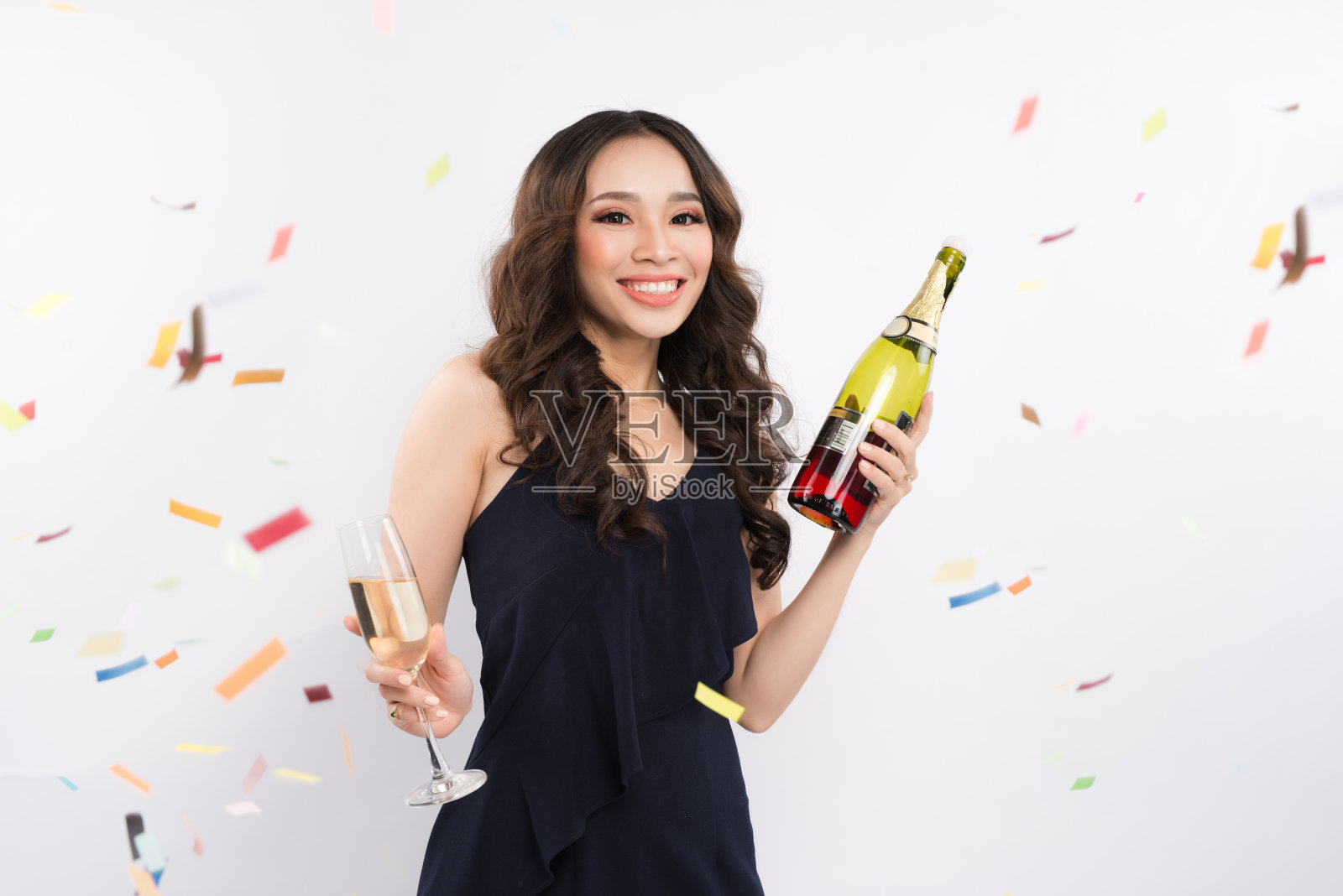 亚洲妇女举着酒瓶庆祝白色背景上的五彩纸屑照片摄影图片
