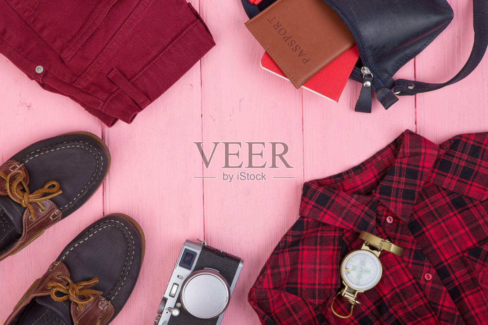 旅游用品-包，牛仔裤，护照，照相机，指南针，鞋子，衬衫，笔记本在粉红色的木制背景照片摄影图片