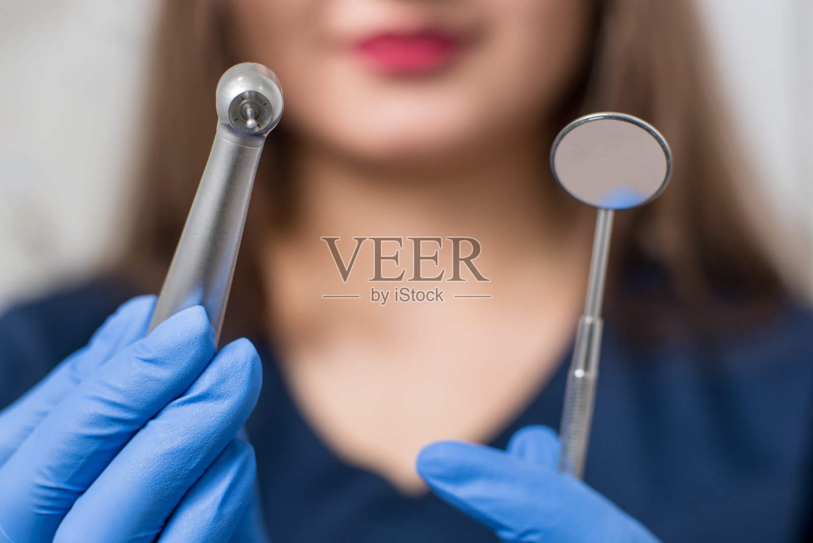 女牙医戴着蓝色手套在牙科诊所拿着牙科设备。特写，选择性的关注工具。牙科照片摄影图片