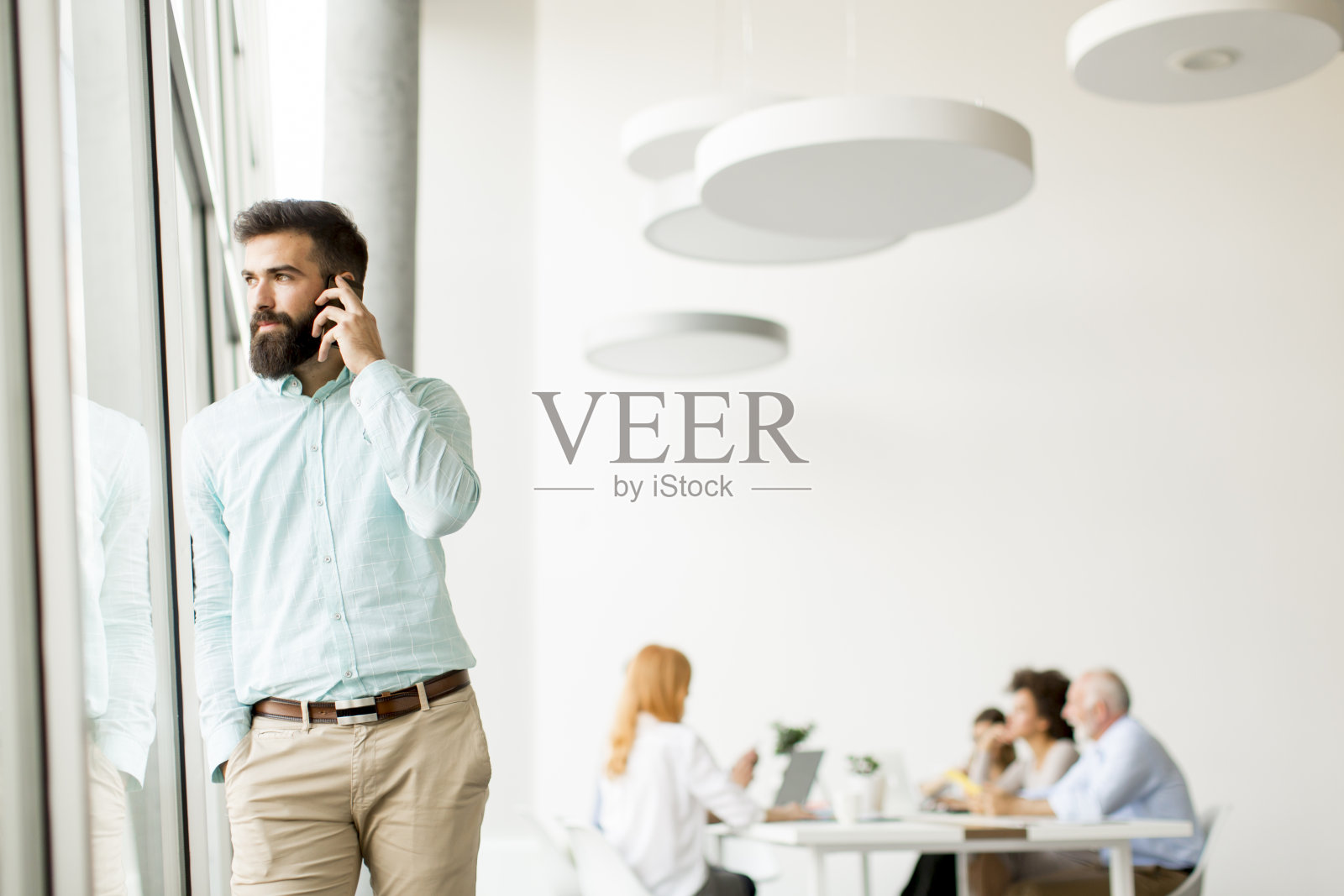 一个年轻的商人在办公室的窗户边讲电话照片摄影图片