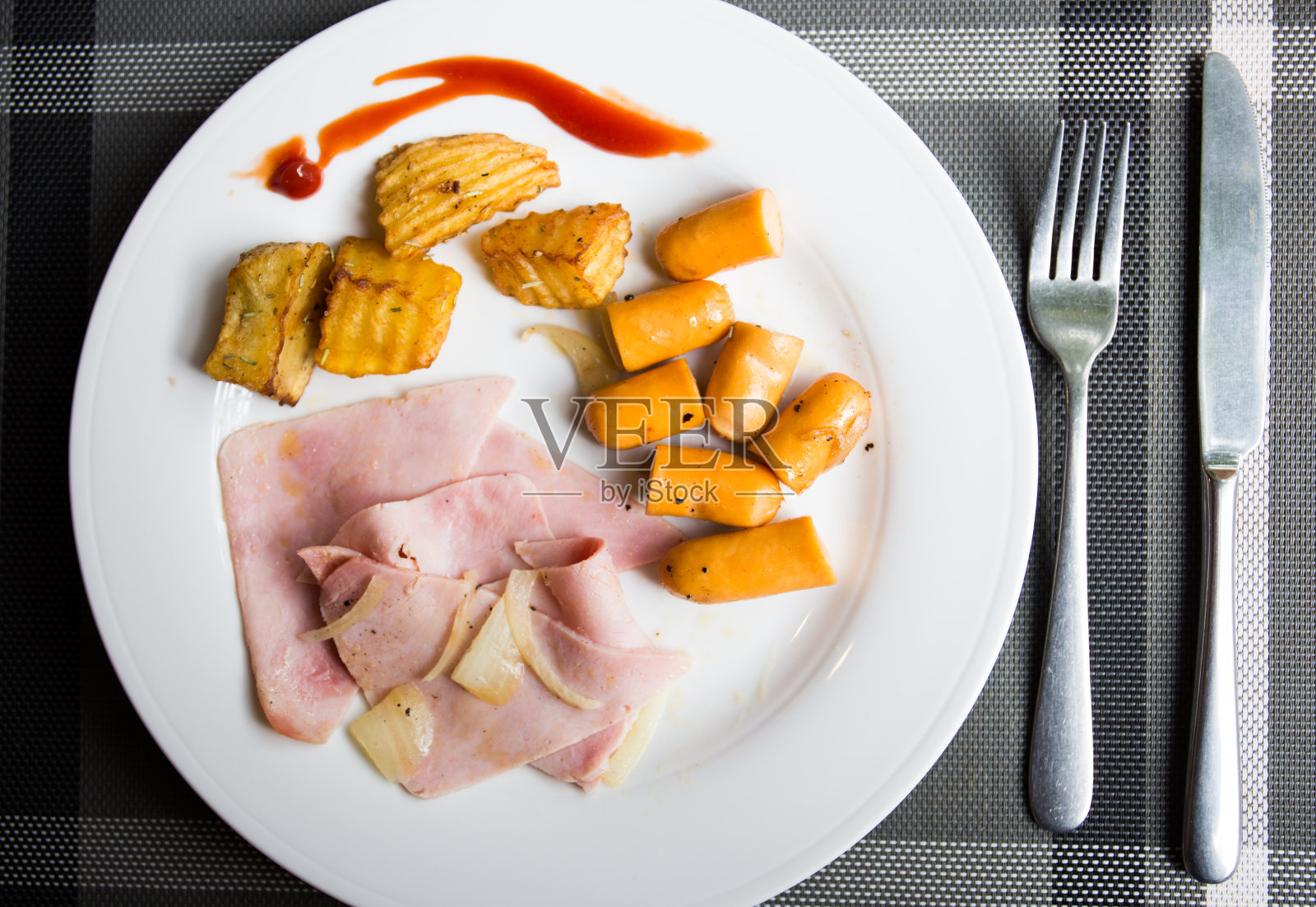 早餐的特写，火腿，热狗，炸薯条和番茄酱，叉子和牛排刀放在塑料垫子上的木桌上照片摄影图片