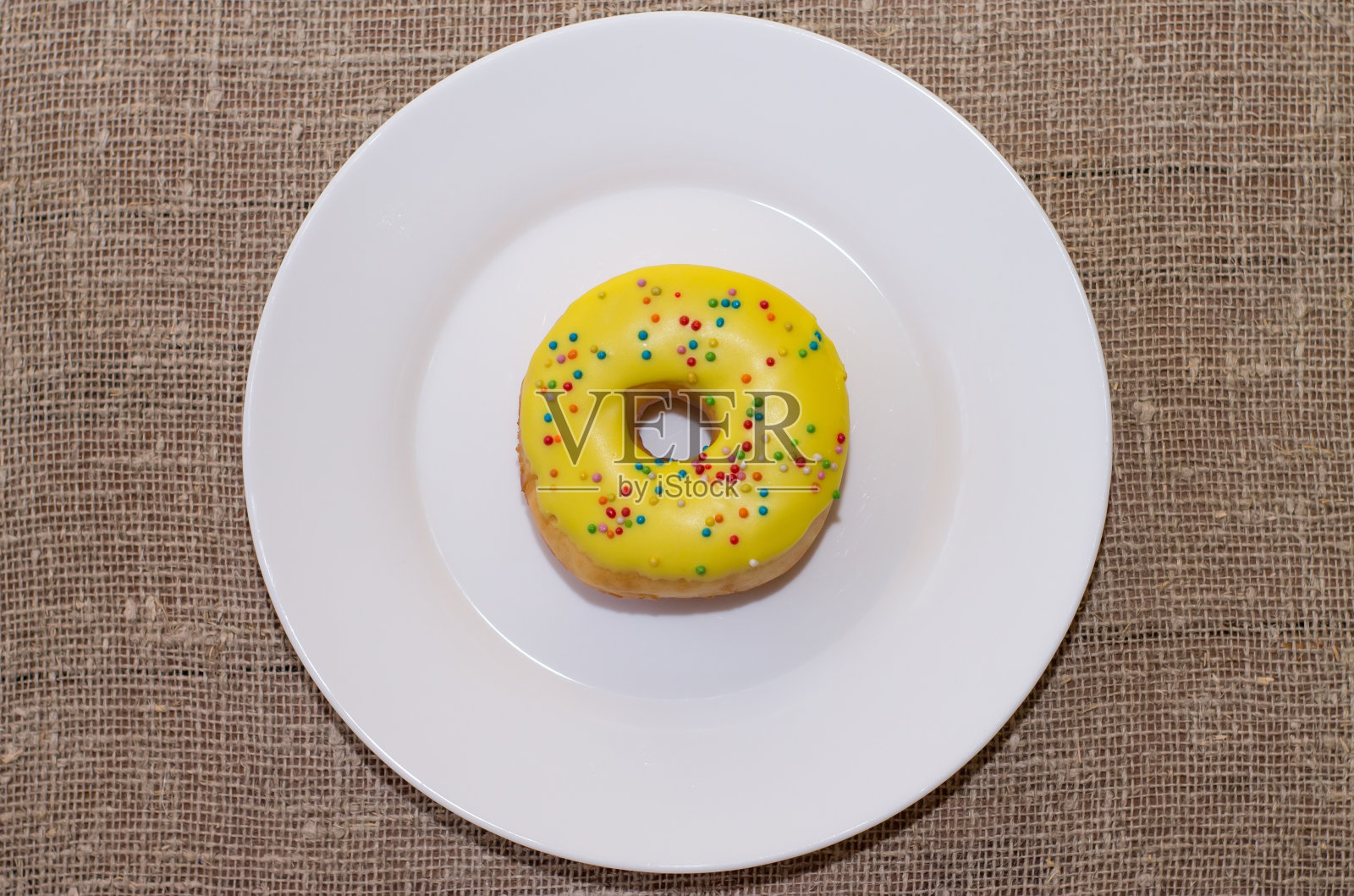 白色盘子上浇了一层糖霜的甜甜圈。彩色的甜蜜的甜甜圈照片摄影图片