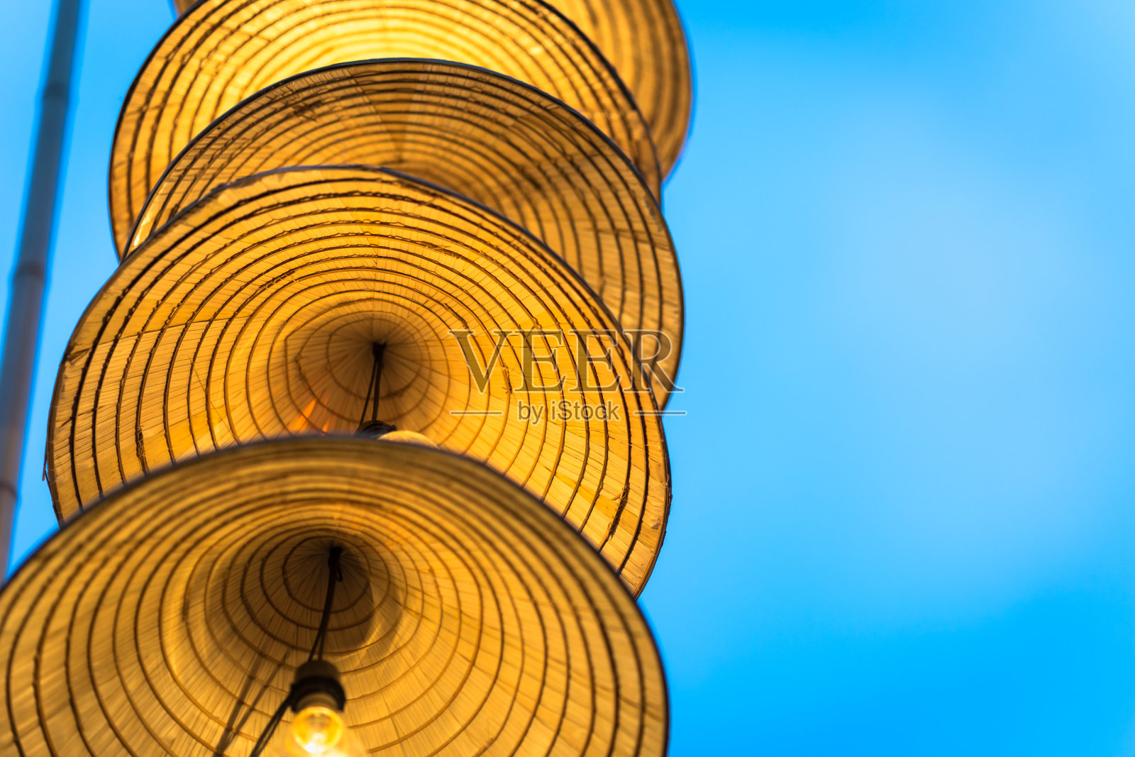 灯饰条纹越南传统圆锥形帽子挂在铁丝上装饰，黄昏时天空湛蓝照片摄影图片