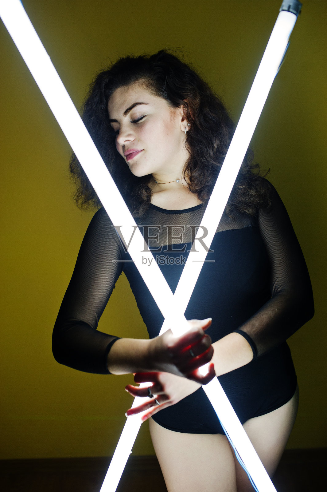 卷毛的黑发加尺寸模型与两个长led灯对着黄色的墙。照片摄影图片