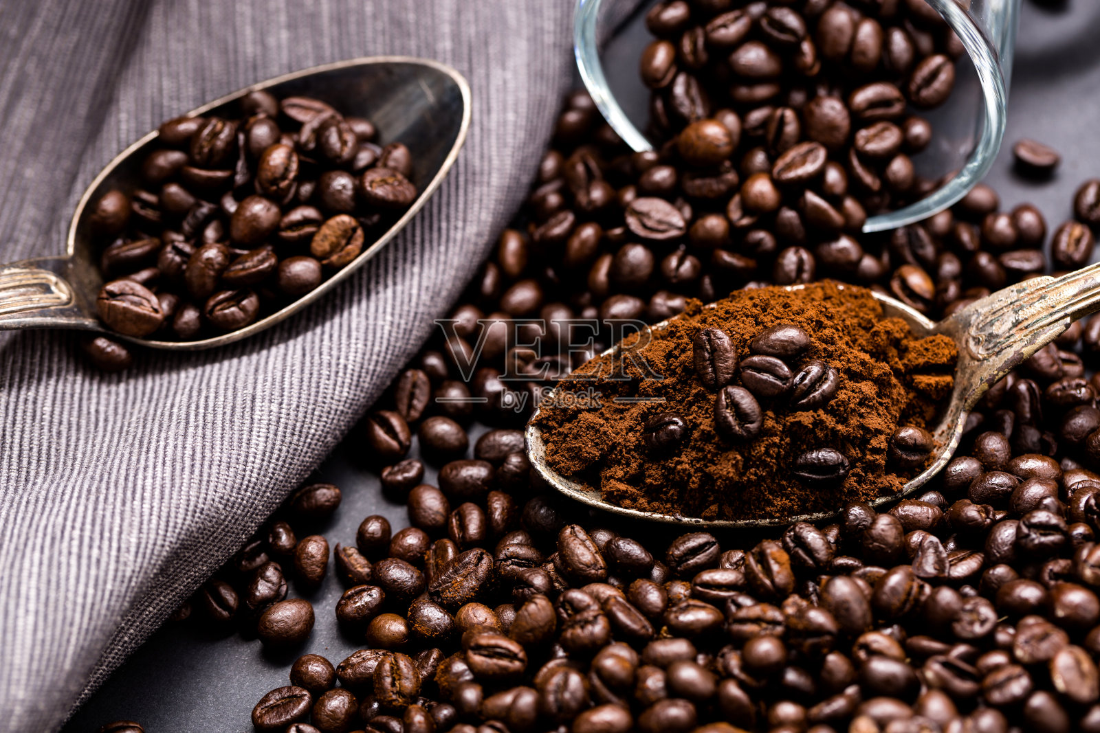 咖啡倒进一个古老的银器勺子里。勺子周围撒满了咖啡豆。照片摄影图片