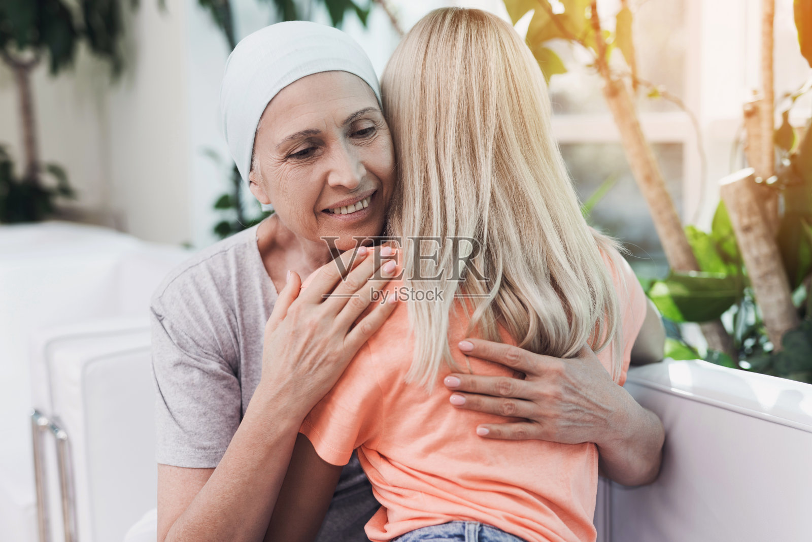 一位身患癌症的妇女坐在白色沙发上，旁边是她的女儿。一个女孩正在拥抱一个女人照片摄影图片
