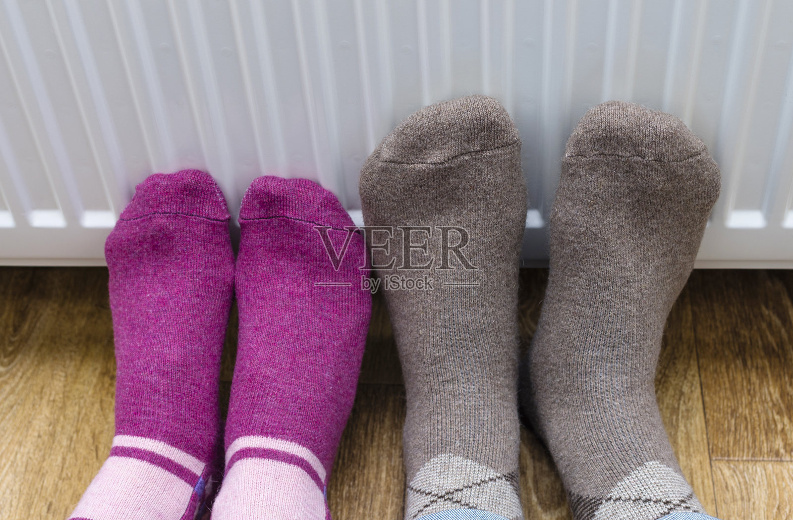 妇女和孩子穿着彩色条纹羊毛袜子在加热器前暖脚照片摄影图片