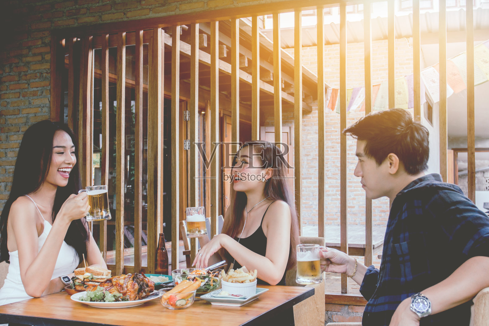 两名亚洲女子和一名男子。喝啤酒，微笑。庆祝派对，快乐饮食概念照片摄影图片