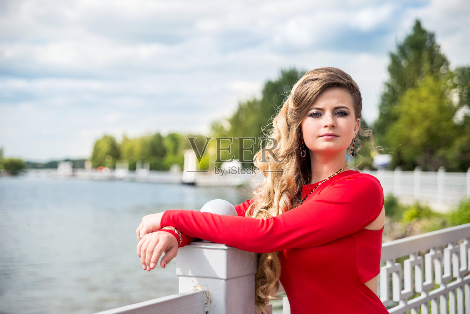 在夏天的湖边，穿着红色连衣裙的微笑女人的肖像照片摄影图片