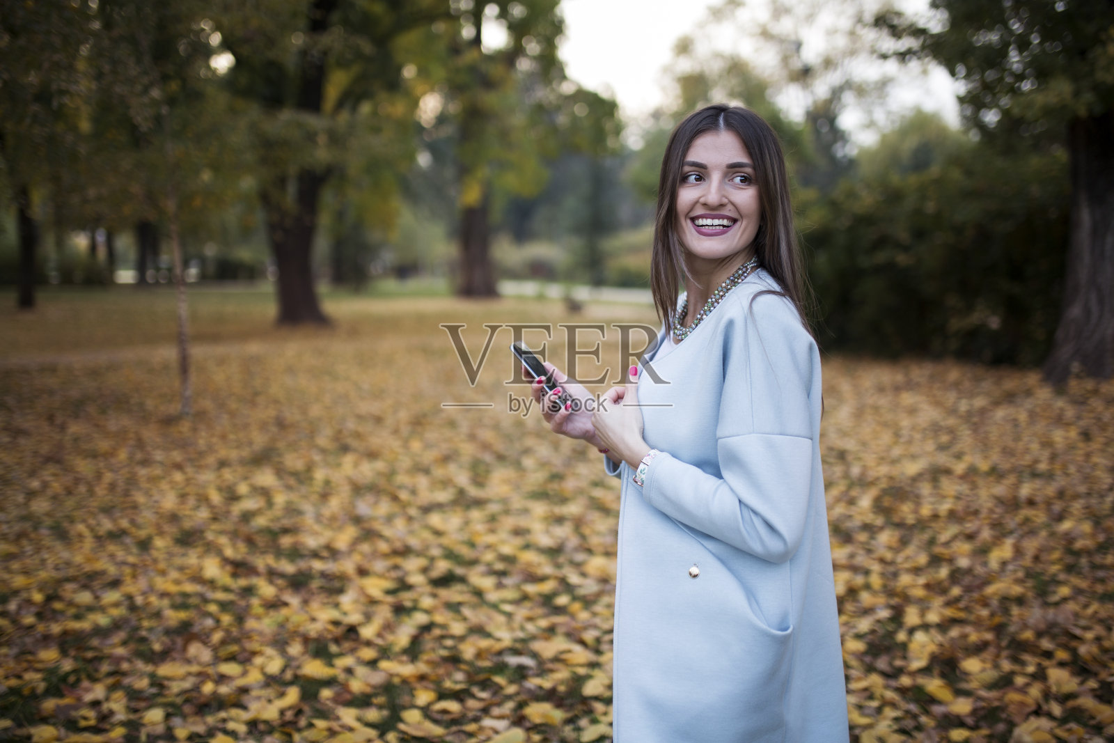 可爱的深褐色的女人使用手机在一个公园秋天照片摄影图片