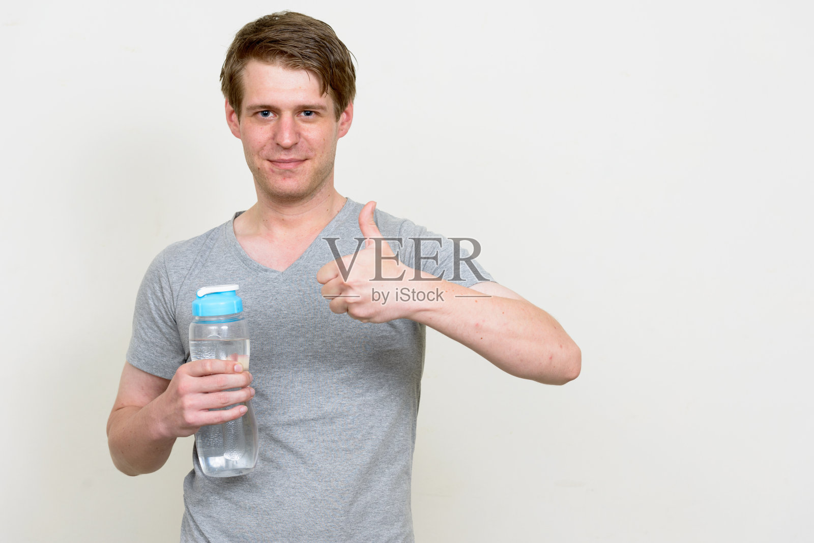 年轻英俊的男子穿着灰色衬衫准备在白色的背景下去健身房照片摄影图片