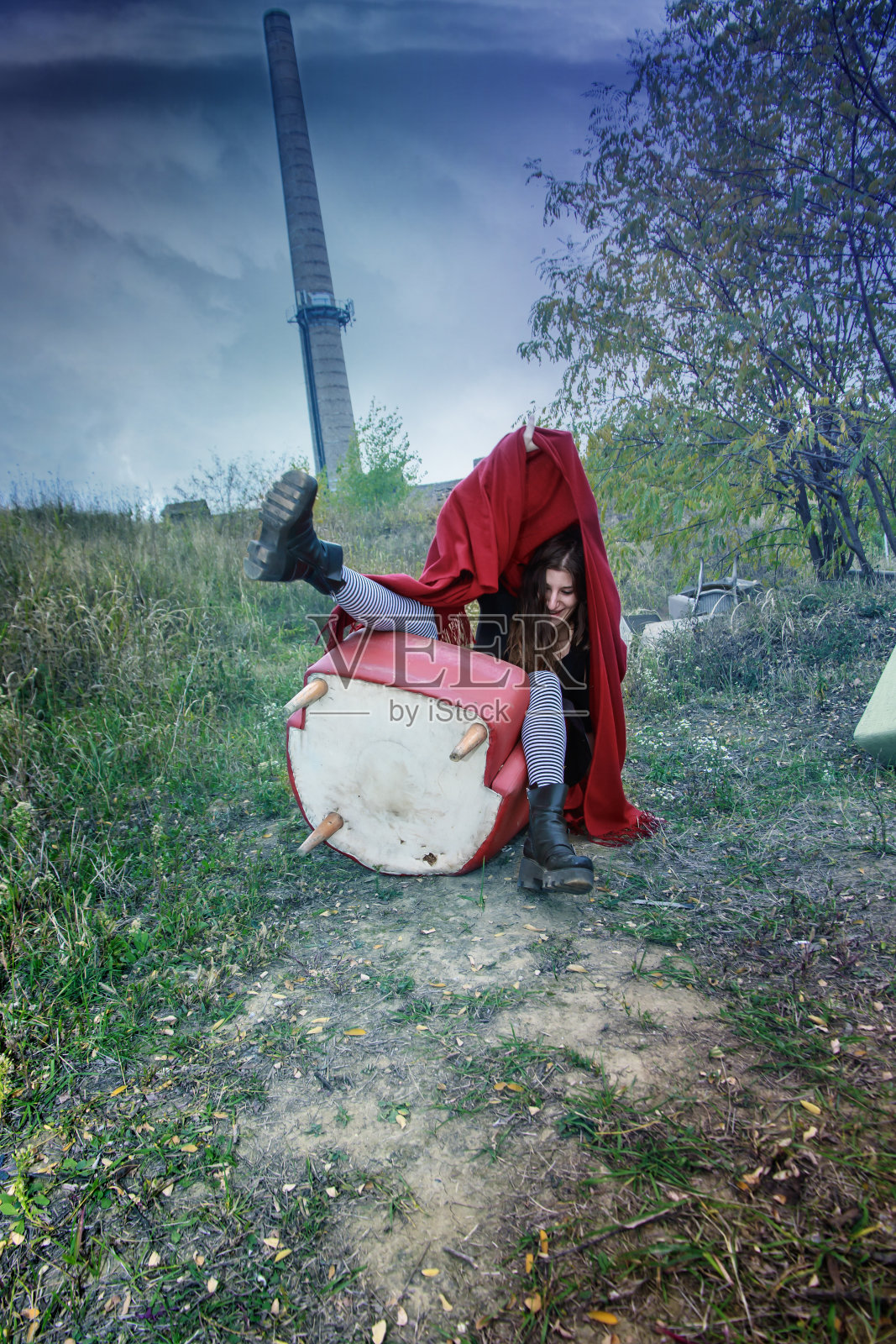 快乐的小丑女孩穿着红色的雨披坐在椅子上照片摄影图片