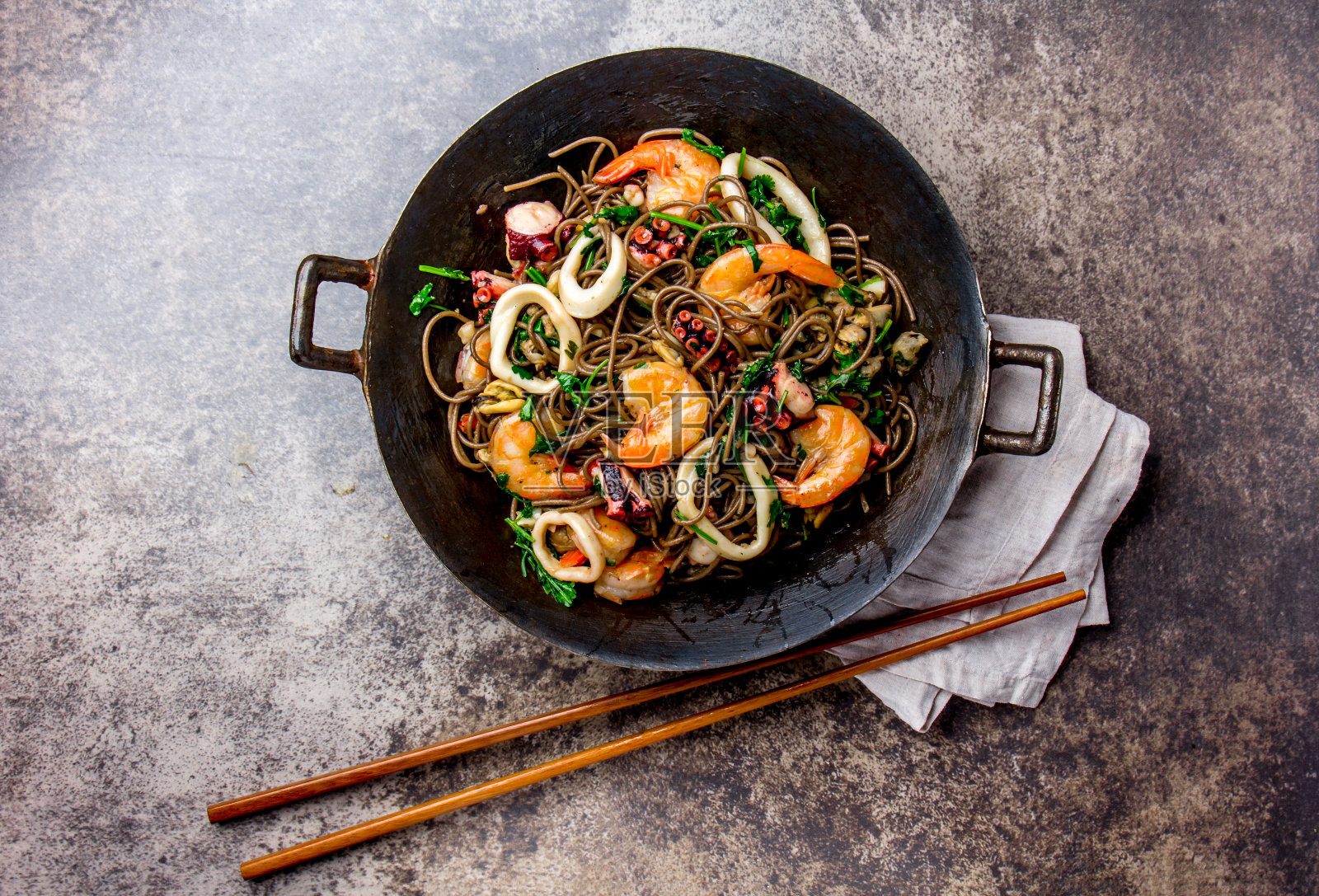 荞麦炒面海鲜-虾，章鱼，鱿鱼在铸铁亚洲炒锅与烹饪筷子。俯视图，石头背景照片摄影图片