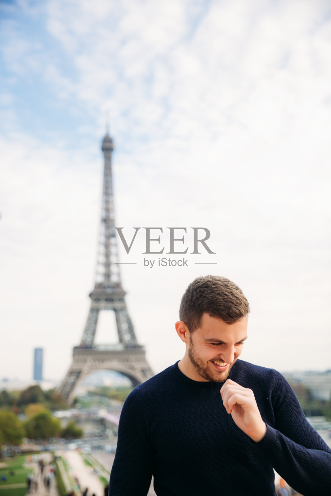 一个穿着深蓝色夹克的年轻人站在埃菲尔铁塔的背景上。晴朗的天气是秋天照片摄影图片