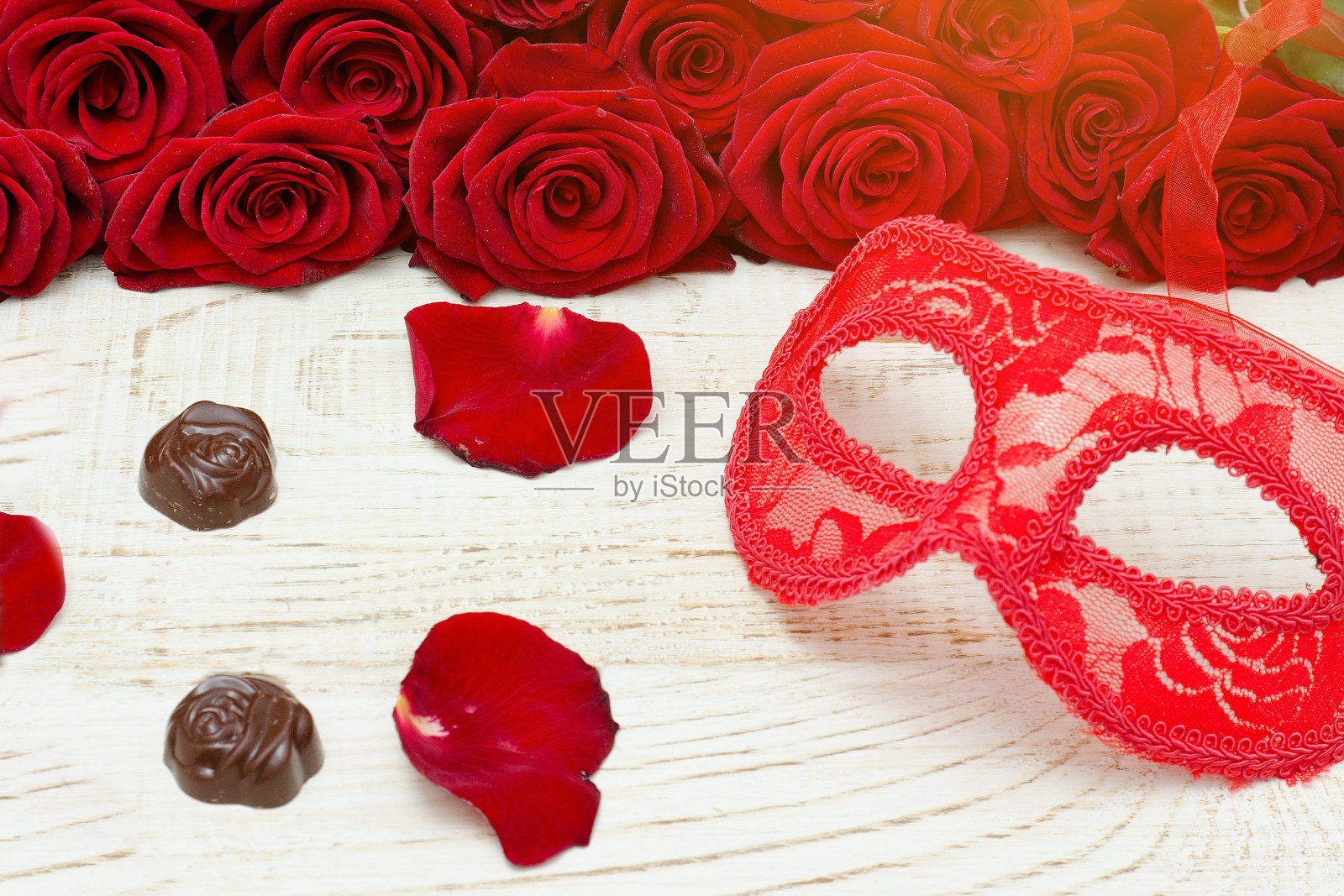 木桌上的红色狂欢节面具和糖果，背景是猩红色玫瑰照片摄影图片