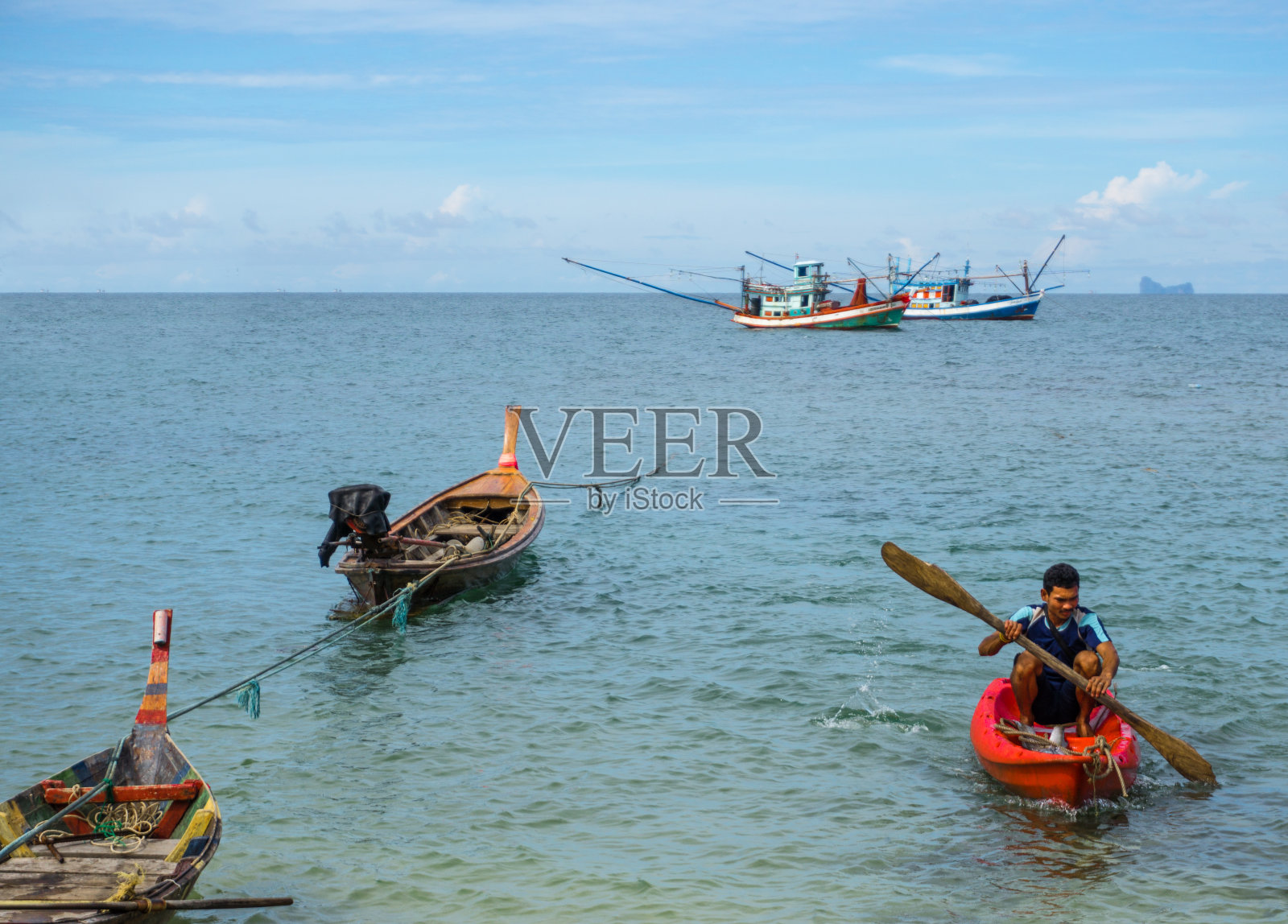 男子在长尾船和商业渔船上划皮划艇照片摄影图片
