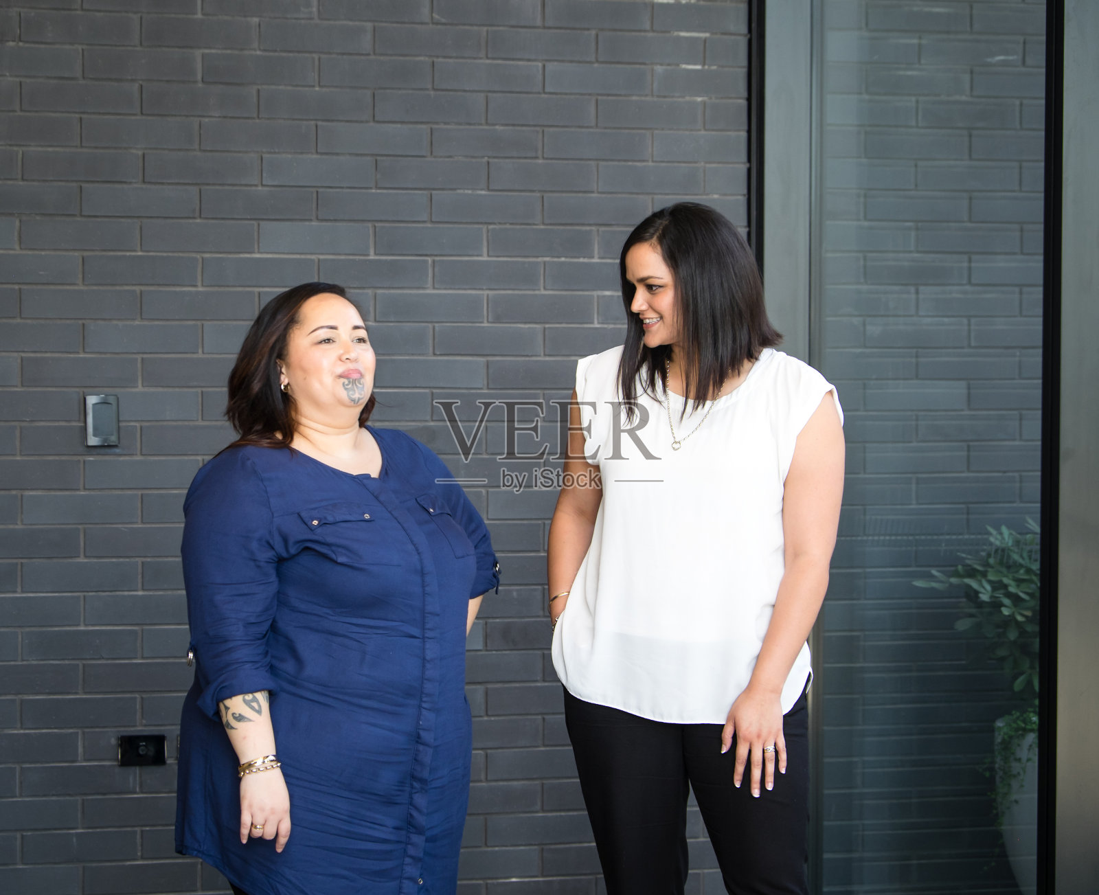 两个毛利妇女-朋友，同事或同事-在办公楼的墙壁边聊天。照片摄影图片