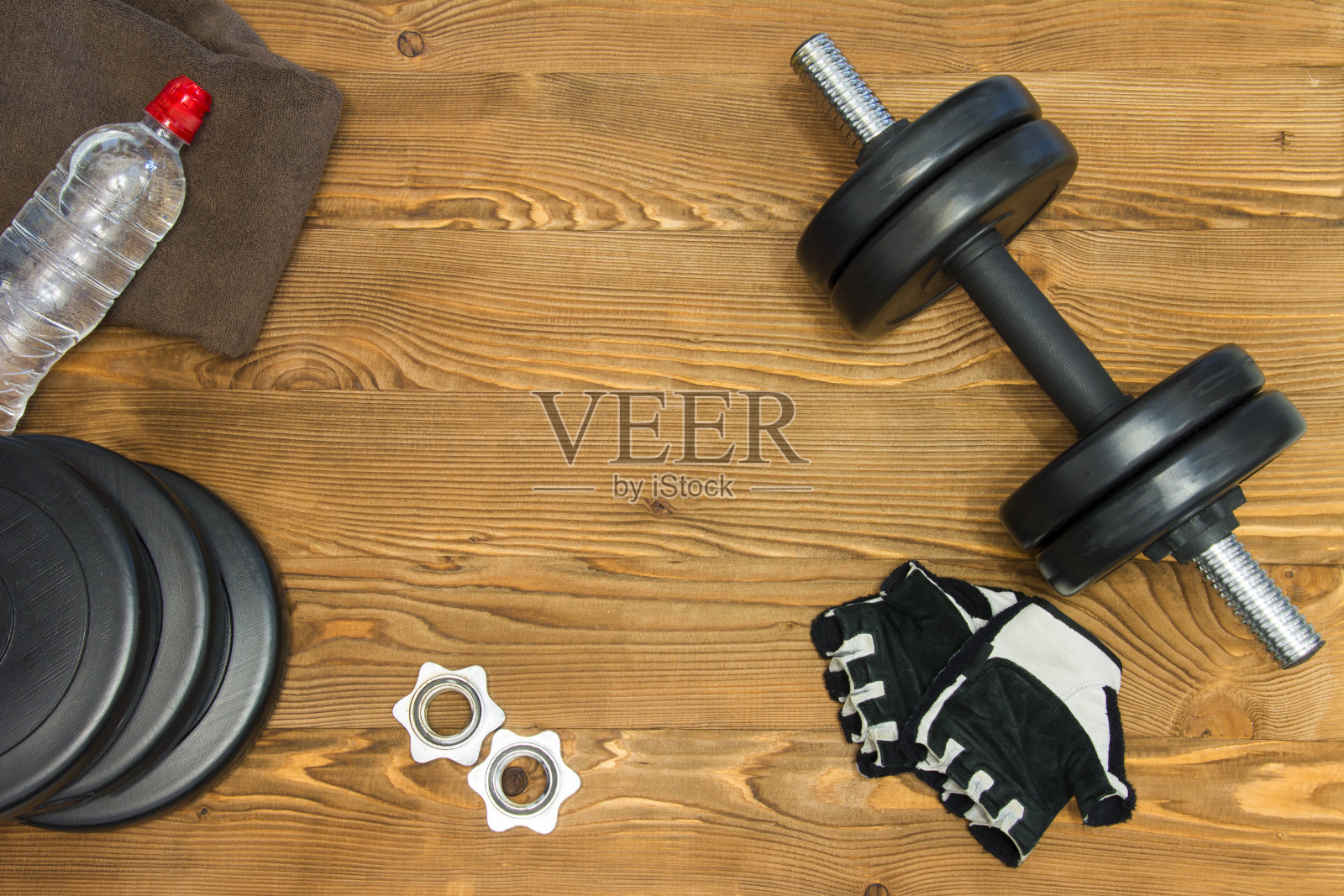 运动和运动的概念。木制背景上的哑铃、手套、毛巾和瓶装水照片摄影图片