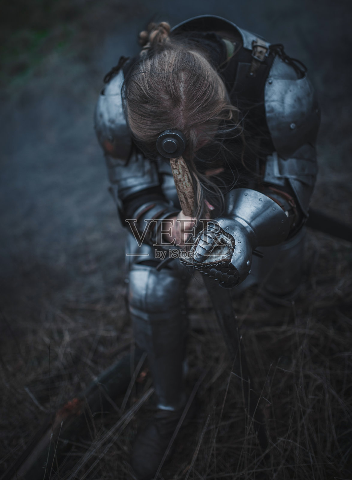 《贞德》中的女孩身穿盔甲，手握宝剑，跪在干草的背景下。照片摄影图片