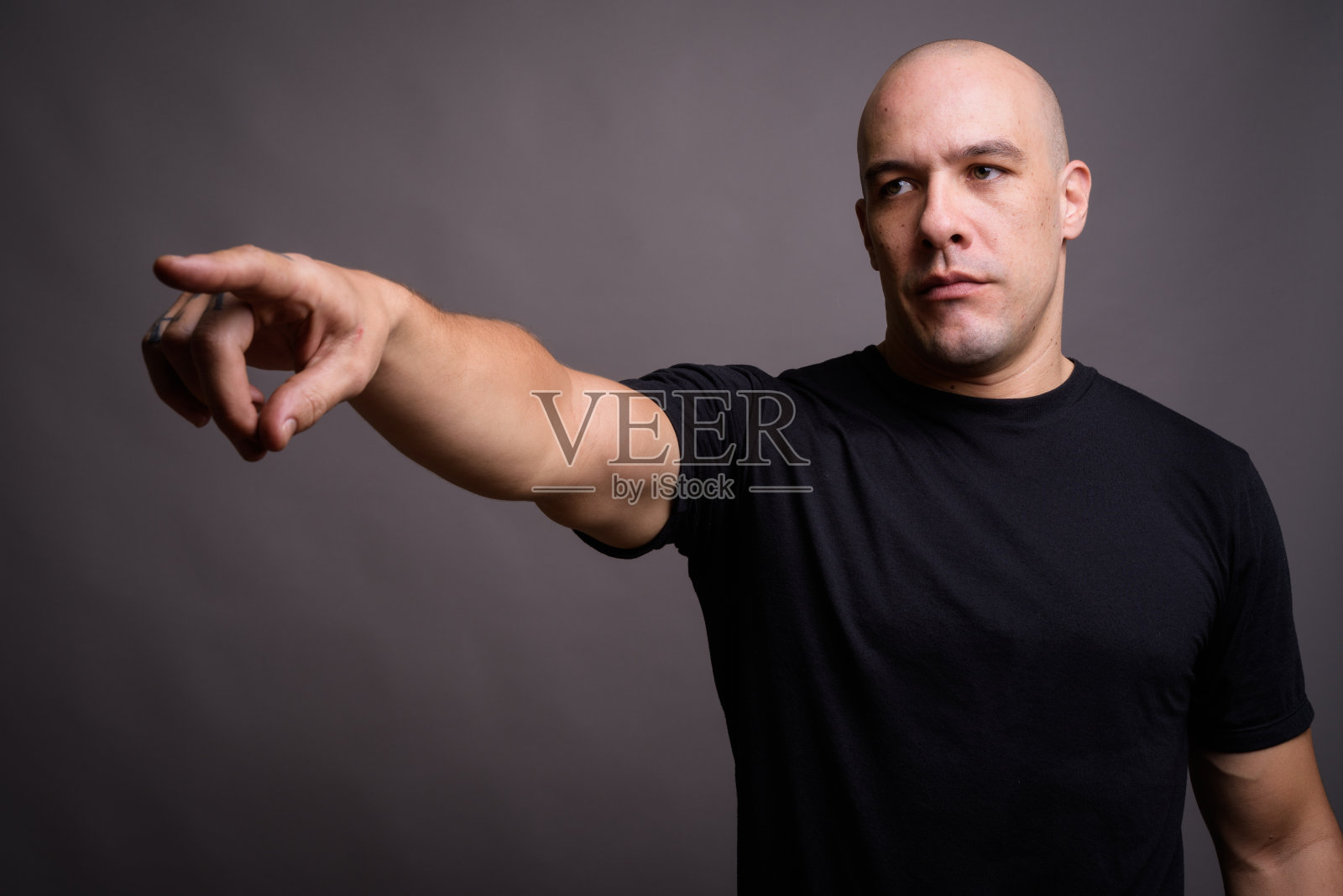 摄影棚里的一个肌肉发达的秃顶男人穿着黑色衬衫，背景是灰色照片摄影图片