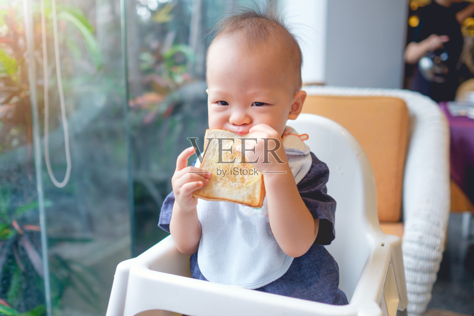 可爱的亚洲小男孩18个月/ 1岁的蹒跚学步的婴儿男孩咬和吃吐司作为早餐照片摄影图片