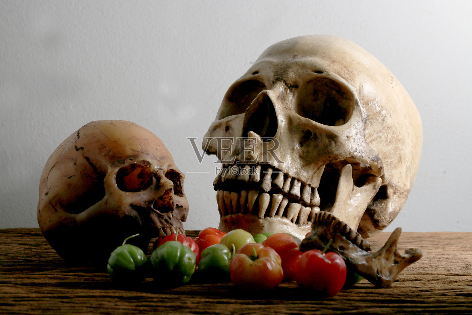 人类头骨和收获时新鲜樱桃的静物照片放在木桌上，以墙壁为背景。照片摄影图片