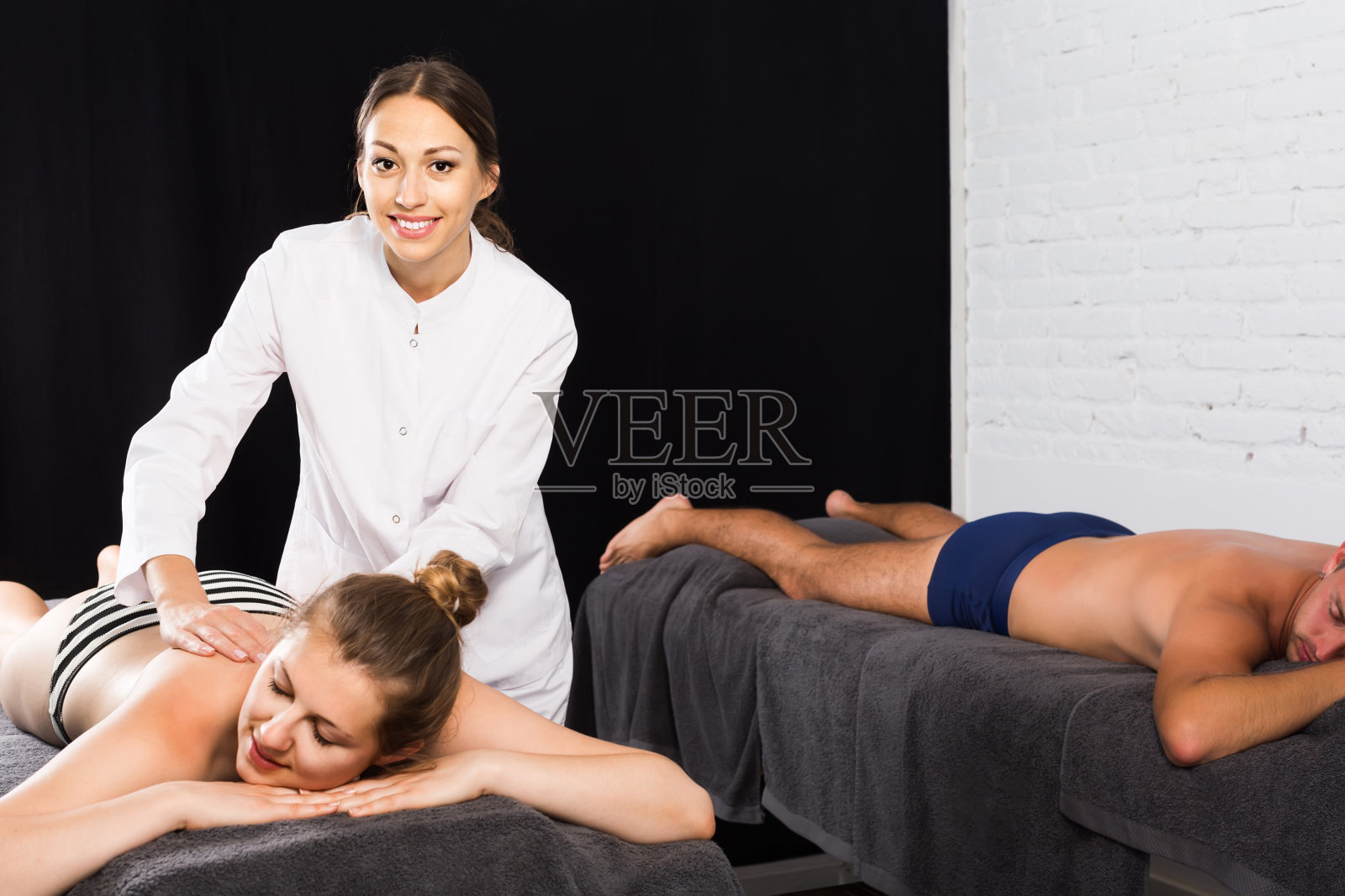 女按摩师在背部做按摩年轻的夫妇，谁躺在一个美容院的按摩表女按摩师在背部做按摩年轻的夫妇，谁躺在一个美容院的按摩表照片摄影图片