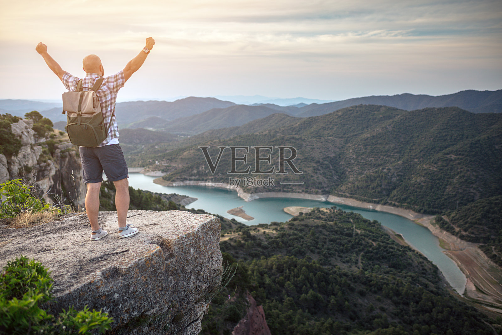 日落时分，一个旅行者站在山顶上，双臂张开。美丽的山景展现在他面前。照片摄影图片