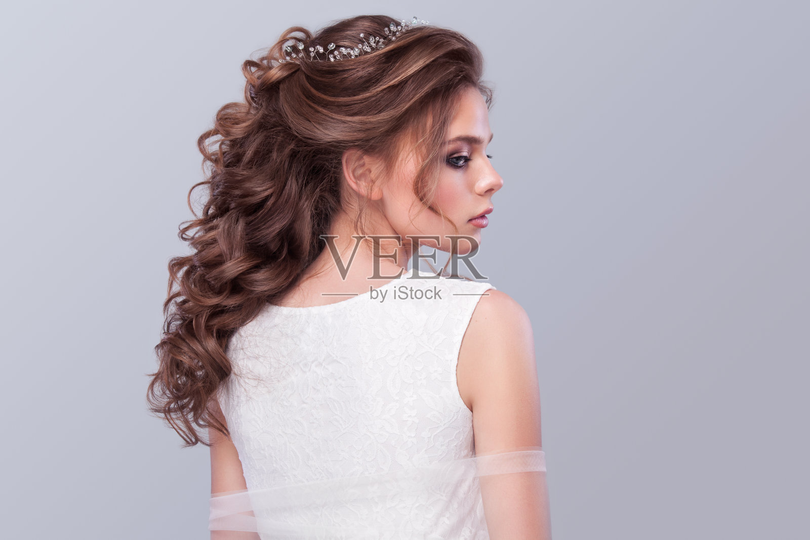 美丽的新娘与时尚的婚礼发型-在灰色的背景。年轻美丽的新娘特写肖像。的婚礼。工作室拍摄与复制空间。照片摄影图片
