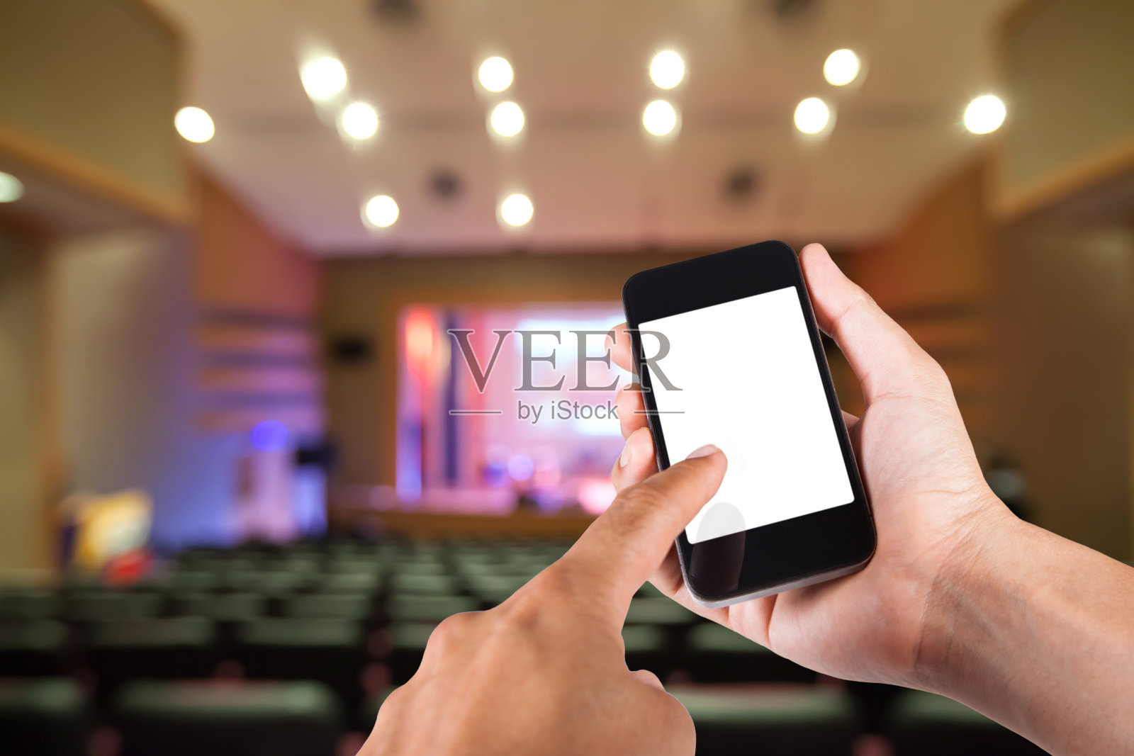 手持智能手机，白色屏幕和剧院模糊的背景。照片摄影图片
