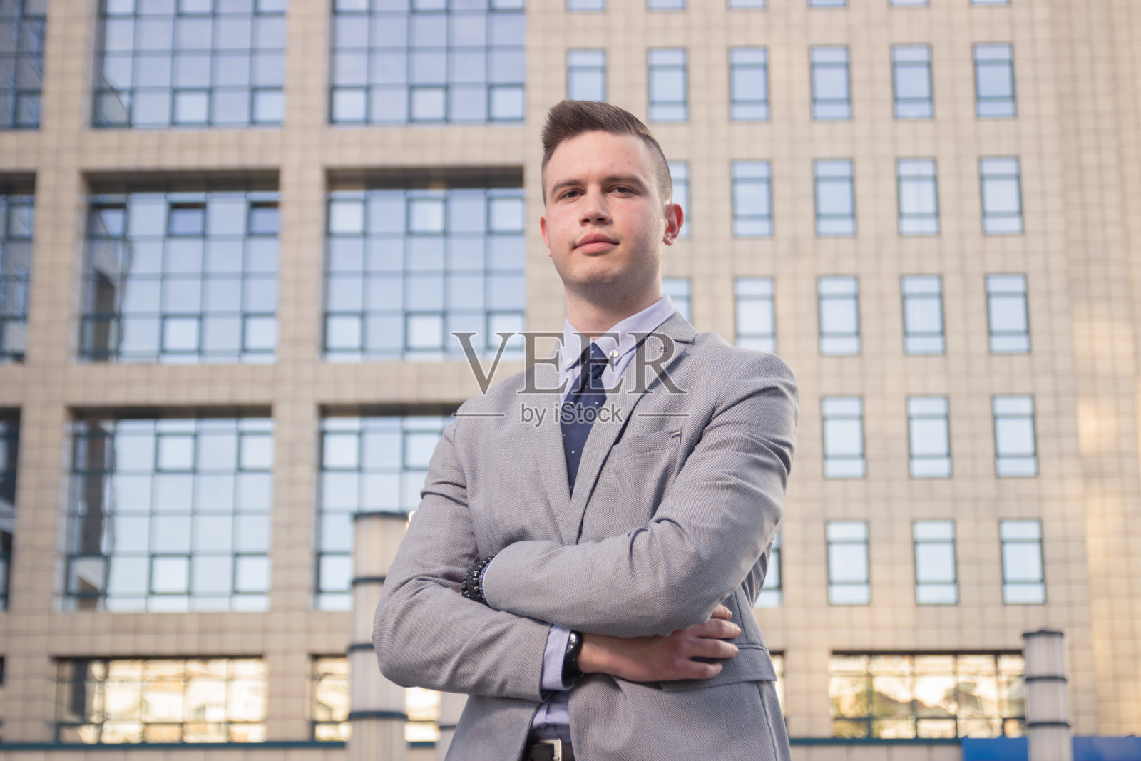 一名年轻的白人男子，面无表情，双臂交叉，西装革履，正装，普通普通人画像，室外建筑物外的窗户后面照片摄影图片