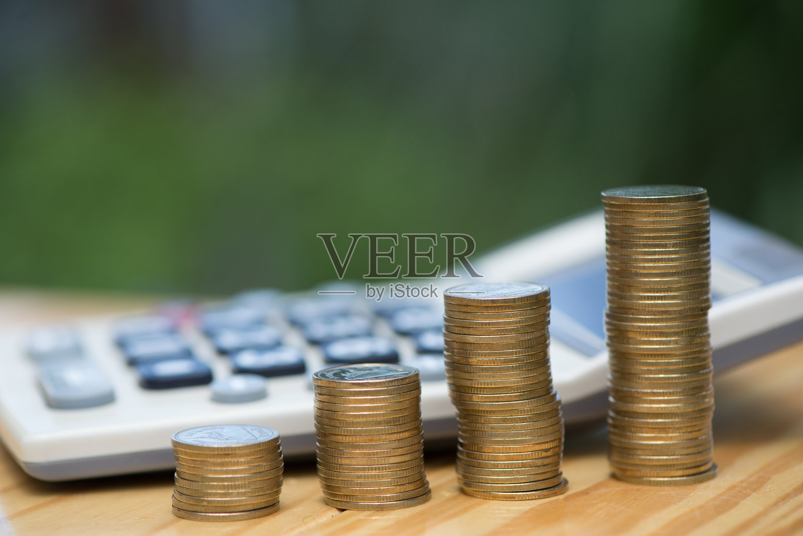 种植硬币和计算器的木材与绿树散焦的背景。照片摄影图片