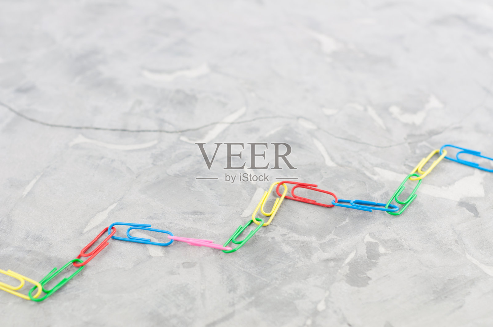 在旧的灰色水泥上排成锯齿形的彩色回形针链照片摄影图片